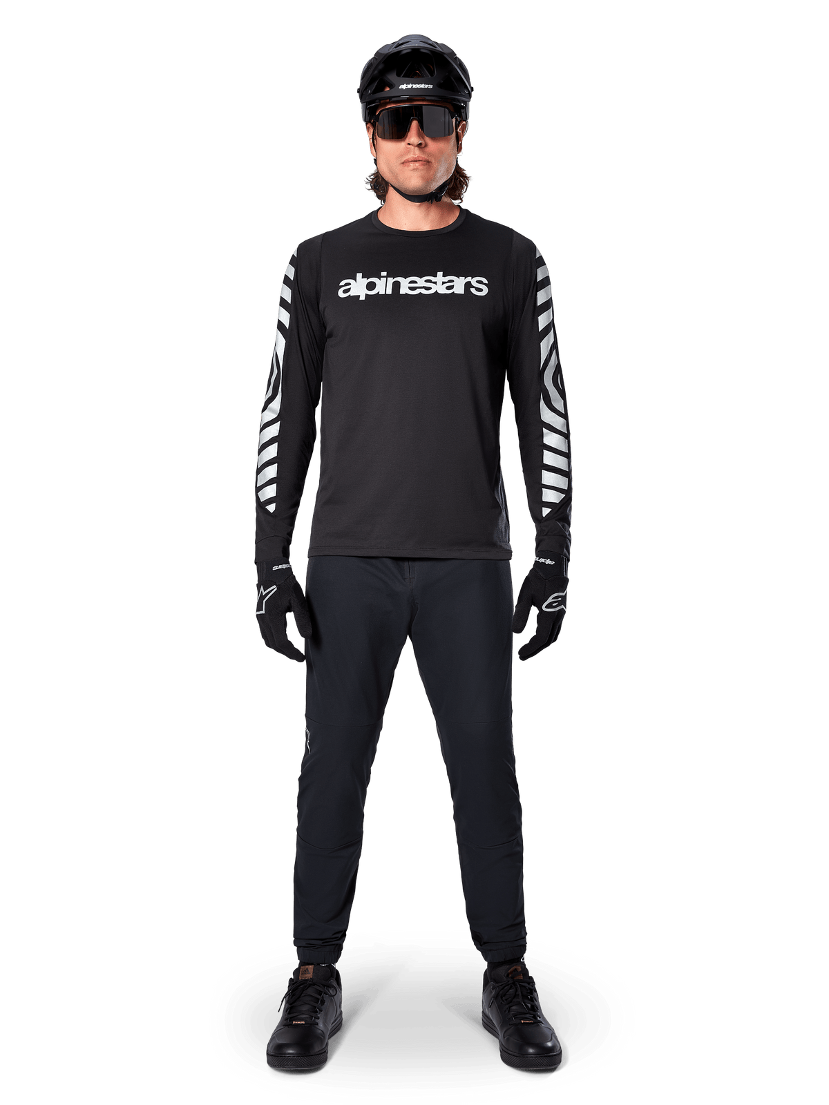 Alpinestars A-Dura Dri Oscar långärmad tröja i Black Reflective, bärs med svart hjälm och solglasögon, med vit logotyp på bröstet och reflekterande grafiska mönster på ärmarna, MTB-utrustning för terrängkörning