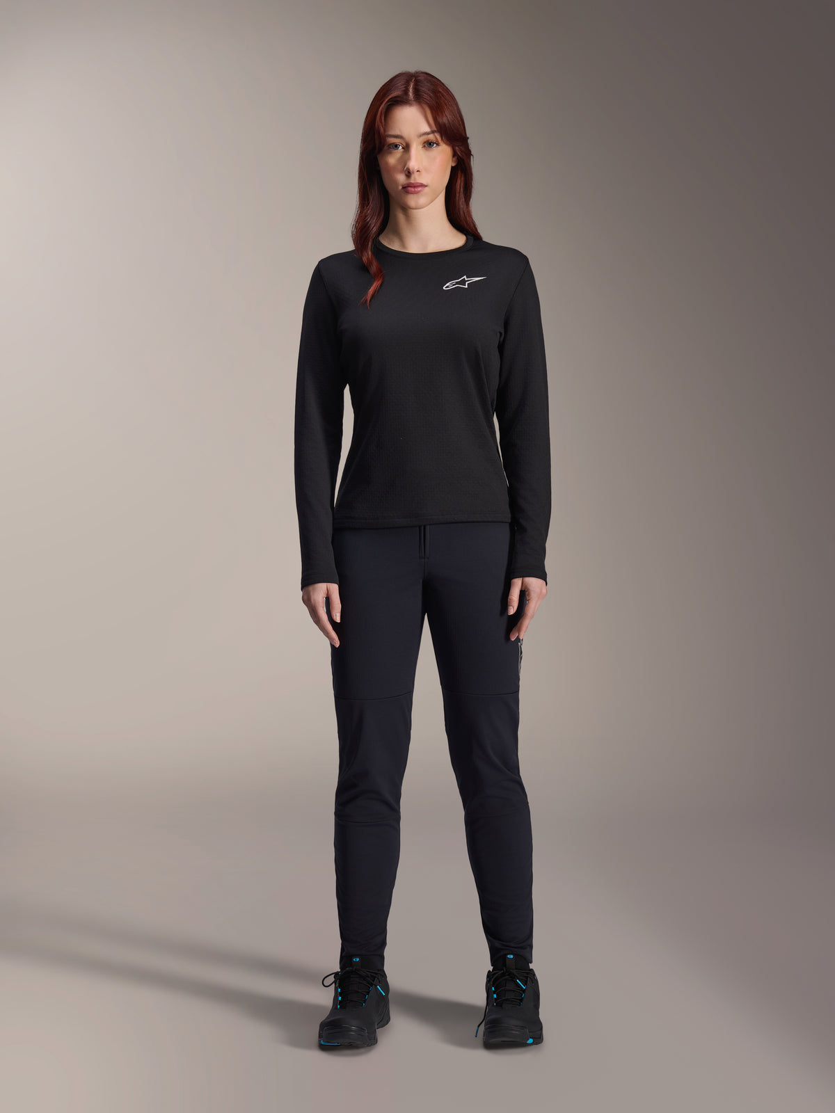 Alpinestars Stella A-Dura Thermal-tröja, långärmad mountainbike-tröja för damer i svart, med en vit logotyp på bröstet, bärs med matchande svart utrustning och cykelskor, studioporträtt.