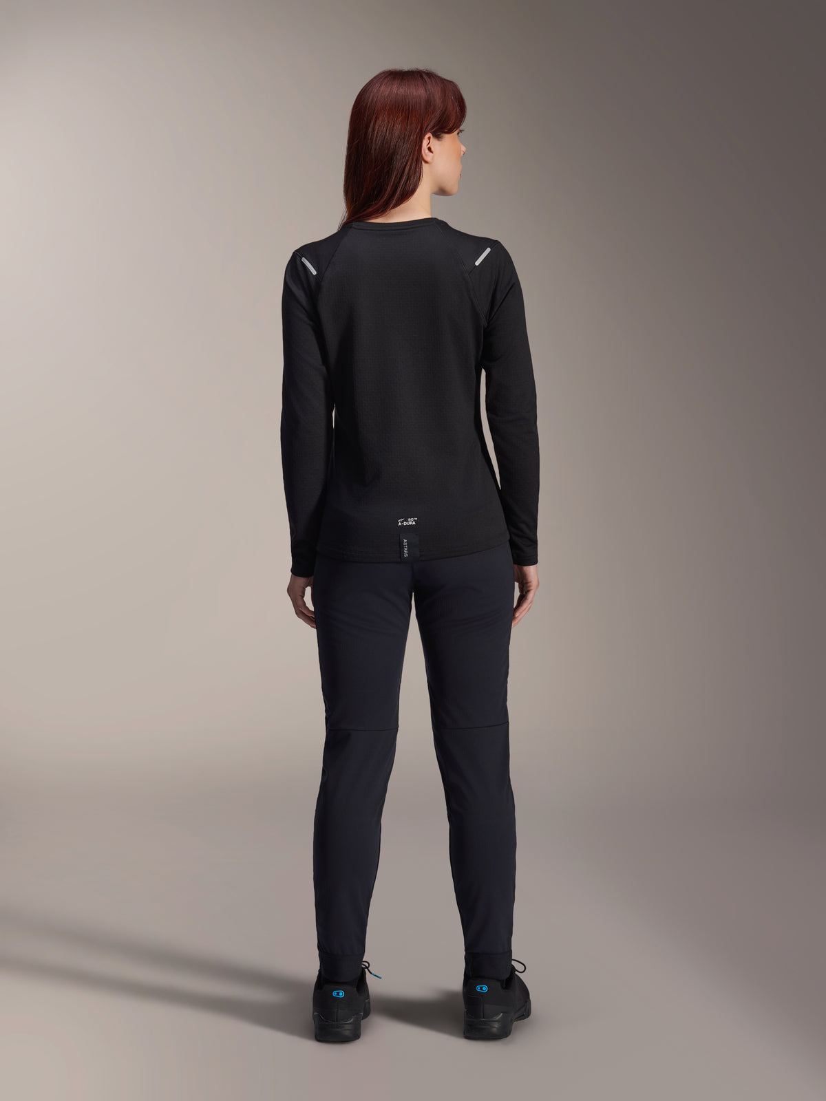 Alpinestars Stella A-Dura Thermal-tröja för dam, vy bakifrån, svart, långärmad cykeltröja med isolerande fleece, bärs med matchande svarta byxor och skor, liten A-Dura-logotyp på nedre ryggen, reflekterande detaljer på axlarna, anpassad för MTB-cykling för damer