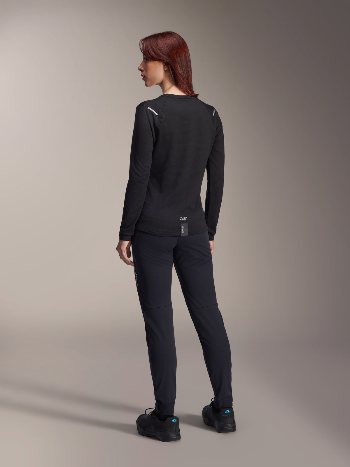 Alpinestars Stella A-Dura Thermal-tröja för damer, långärmad MTB-tröja i svart, vy bakifrån som visar reflekterande detaljer på axlarna och förlängt bakstycke, bärs med svarta byxor och skor, funktionskläder för mountainbike.