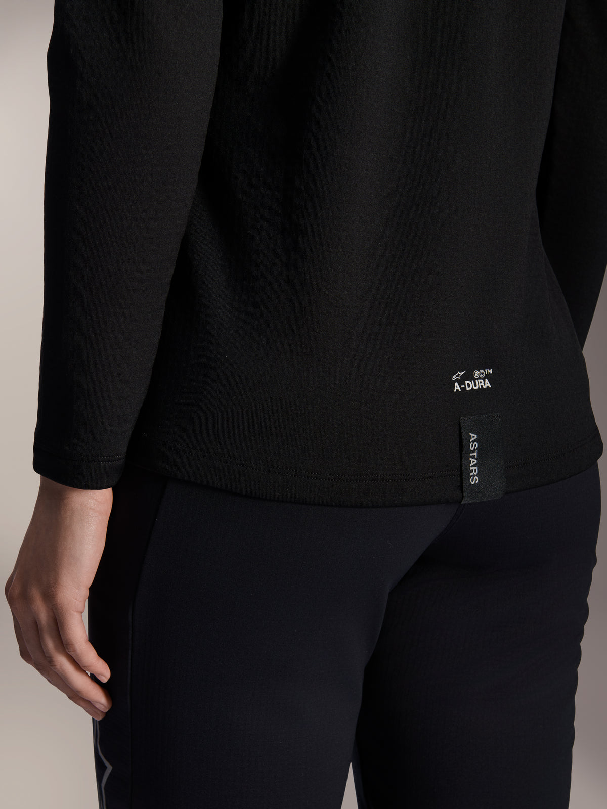 Alpinestars Stella A-Dura Thermal-tröja för dam, svart termotröja för MTB, närbild på nedre fållen baktill med vit A-DURA-logotyp och vertikal ASTARS-logga, designad för mountainbikecykling i kallt väder