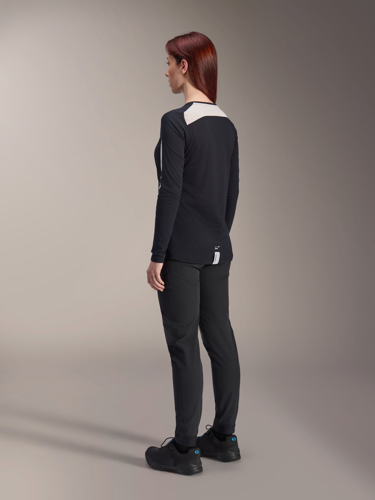 Female rider wearing Alpinestars Women Stella A-Dura Pants and Stella A-Dura Elite Jersey, Black, back view showing white mesh shoulder panels on long-sleeve jersey, slim-fit technical pants, coordinated performance mountain bike gear.