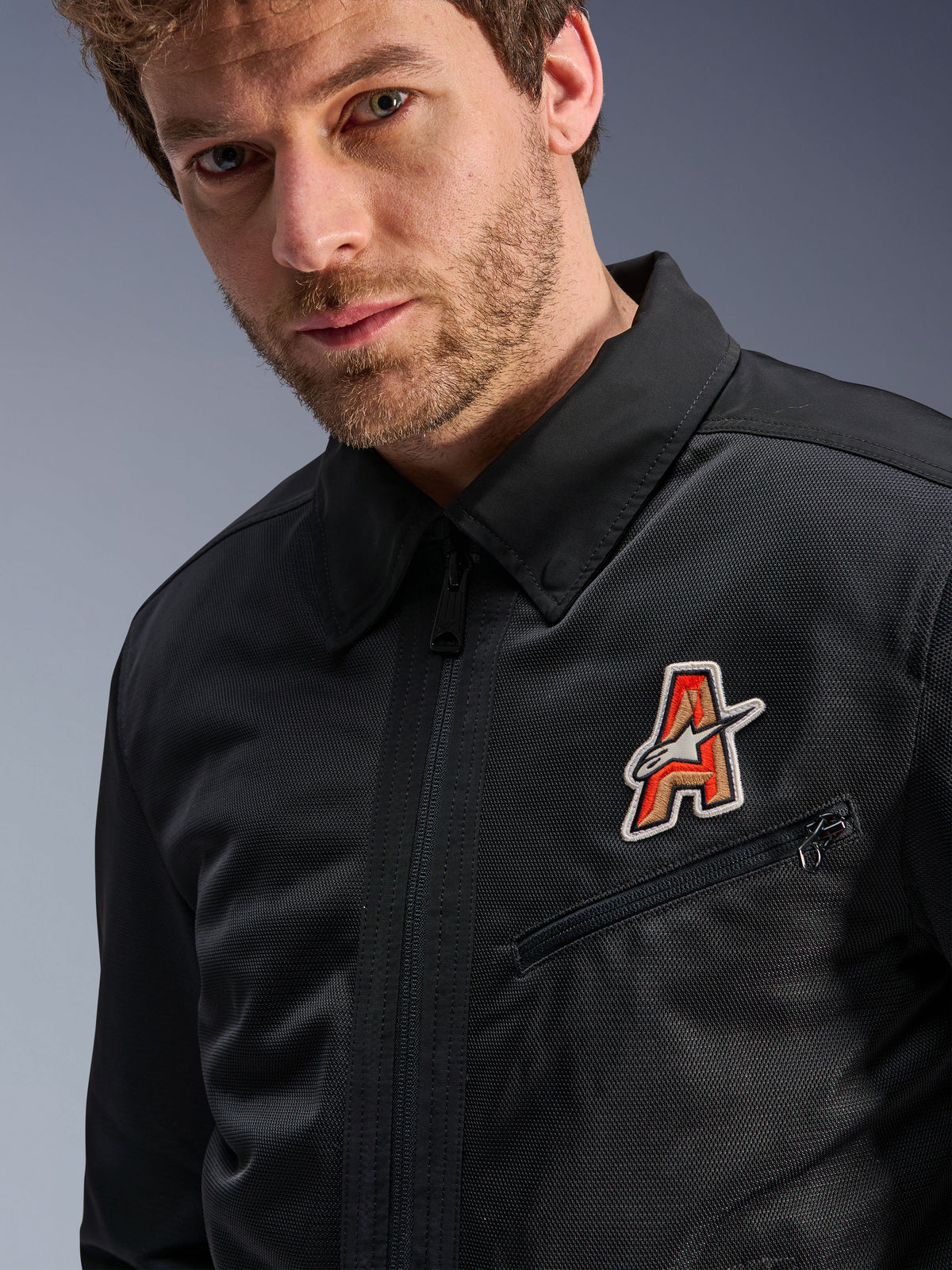 Alpinestars Ignite Air Jacka, svart, med traditionell skjortkrage och ventilerande meshkonstruktion, framhävd av ett rött och guldfärgat 'A'-logomärke på bröstet, bärs av en manlig modell, urban motorcykelutrustning