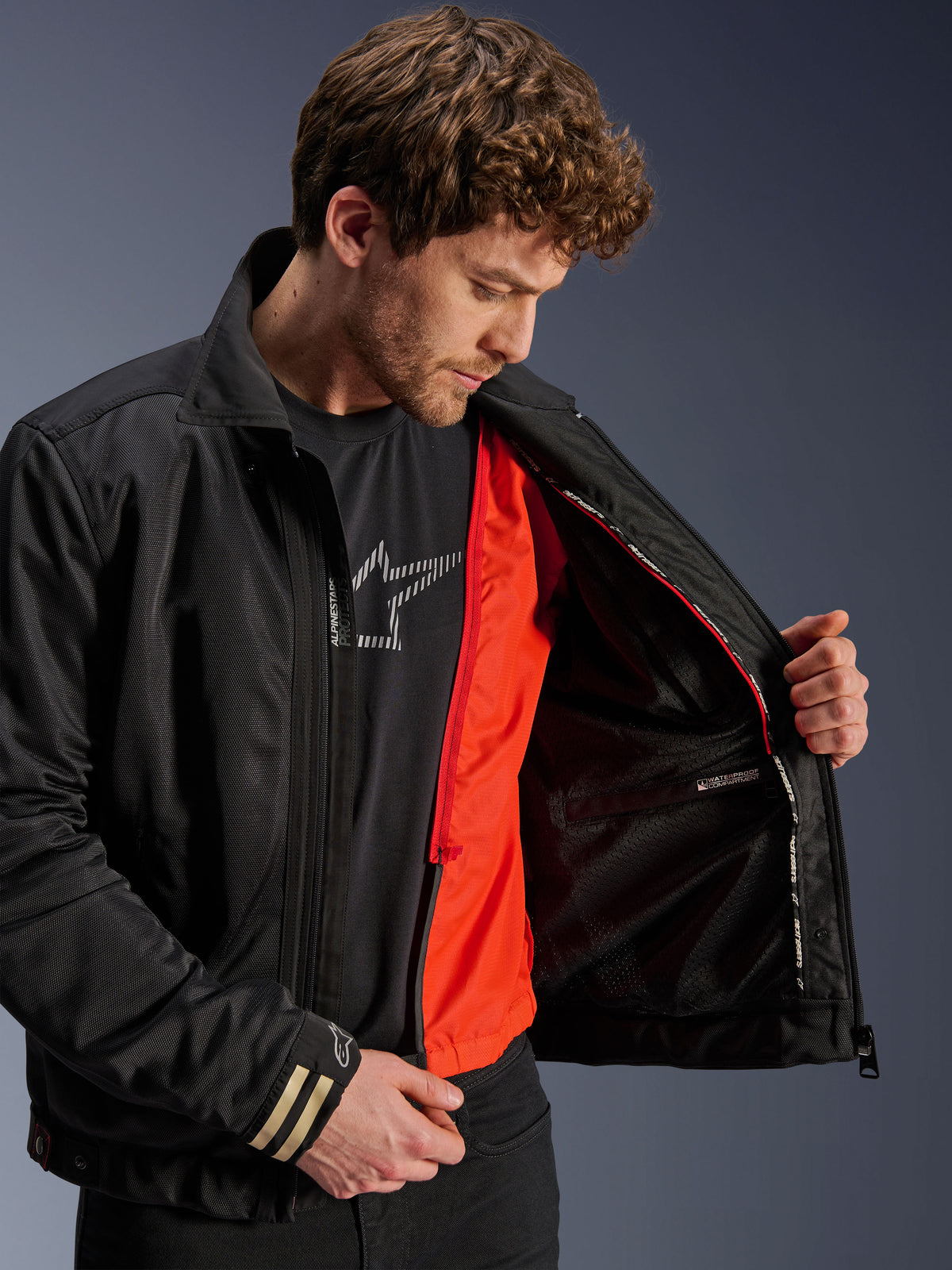 Alpinestars Ignite Air Jacka, svart urban motorcykeljacka med ett klarorange avtagbart vindskyddande foder och mesh-huvuddel, interiörvy som visar ett vattentätt fack, bärs med en svart t-shirt med Alpinestars-logotyp.