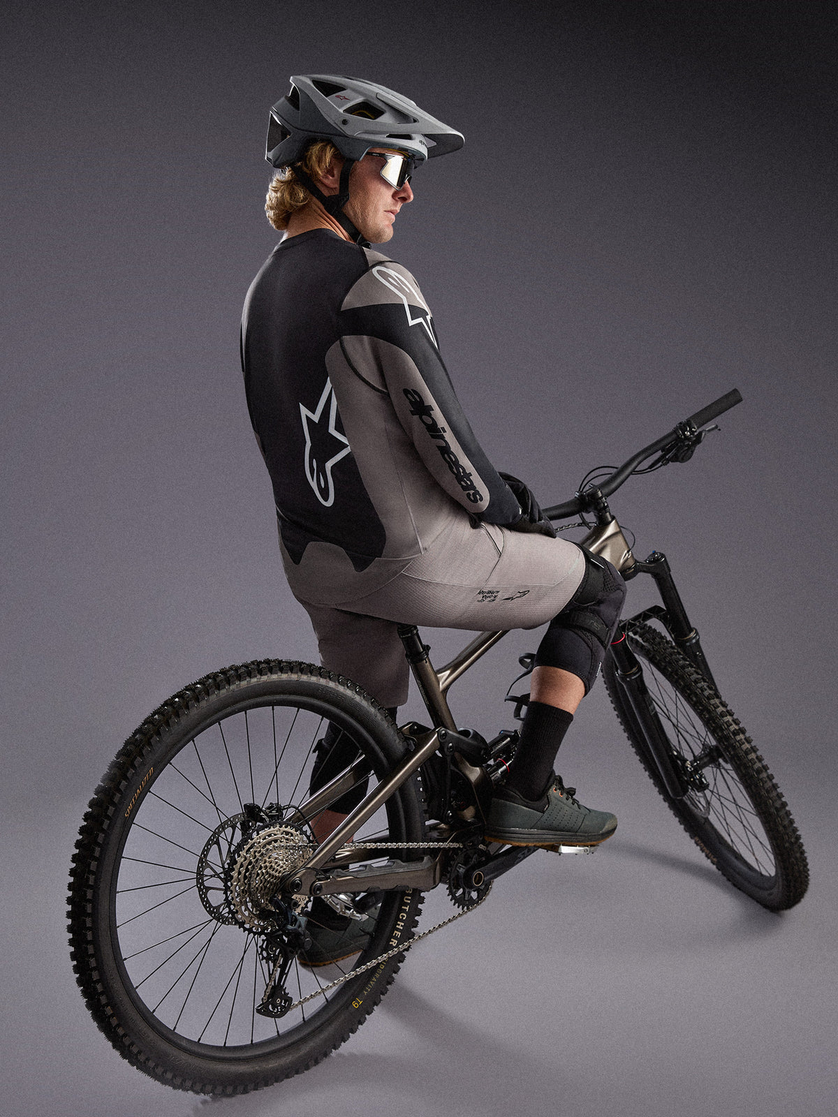 Grå långärmad A-Dura Race-tröja på en mountainbikecyklist, med stora Alpinestars-logotyper och funktionellt stretchtyg.