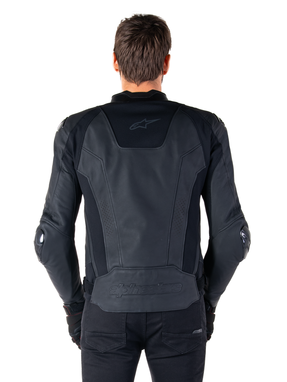 Rear view of a rider wearing the Alpinestars Missile V3 Leather Jacket in black, featuring premium leather construction with technical stretch panels, embossed Alpinestars logo on the lower back, and subtle branding on the upper back, paired with black pants for a coordinated racing sport look.