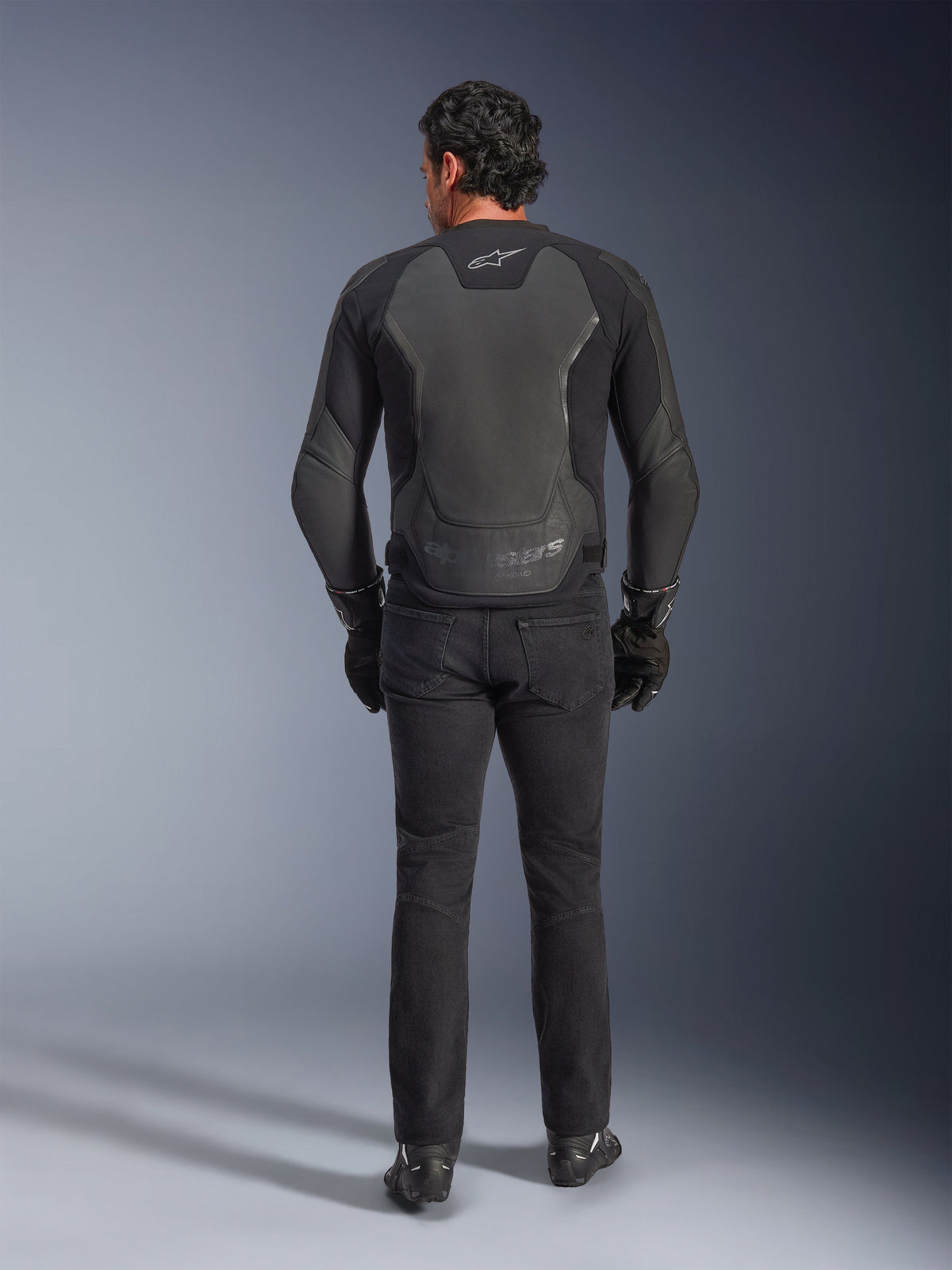 Alpinestars GP Force V2 läderjacka, svart, vy bakifrån, premium sportmotorcykeljacka med läder- och textilkonstruktion, bärs med svarta MC-jeans och handskar, med skyddande axelpaneler och logotypdetaljer