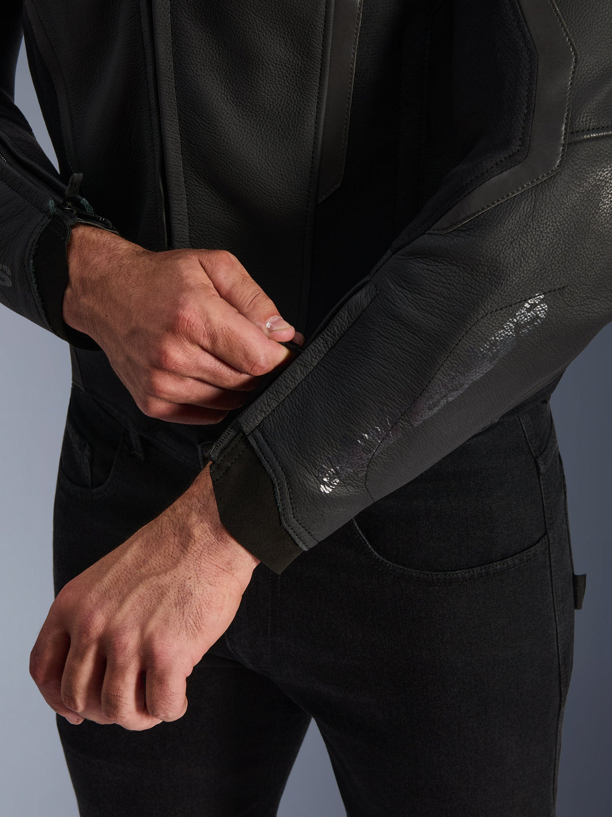 Alpinestars GP Force V2 läderjacka, svart, närbild av den ergonomiska ärmmanschetten, person som justerar handledsstängningen, premiumkonstruktion i nötläder med tekniska detaljer för sportmotorcykelkörning