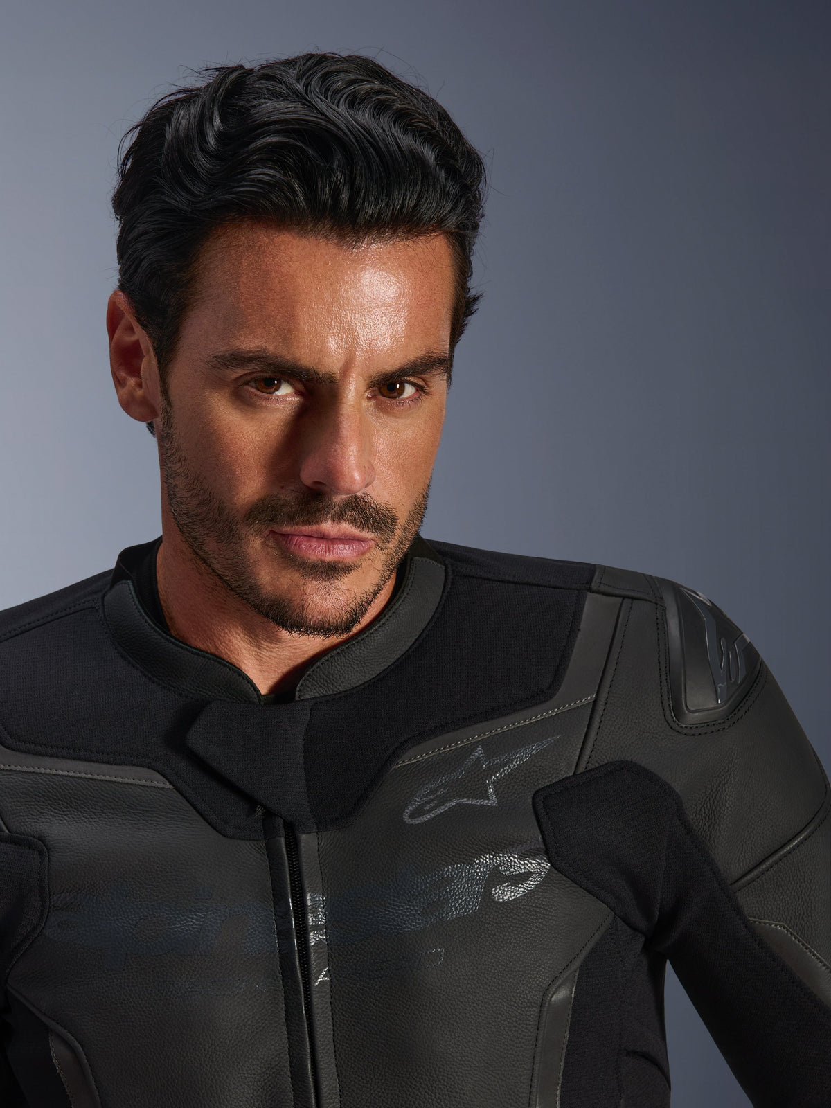 Närbildsporträtt av en manlig modell som bär Alpinestars GP Force V2 läderjacka, svart, med konstruktion i premium nötläder, stretchpaneler i textil och en diskret Alpinestars-stjärnlogotyp, stilren sportfokuserad design för vägkörning.