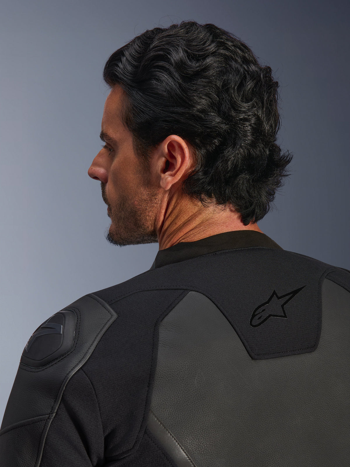 Alpinestars GP Force V2 läderjacka, svart, närbild bakifrån, med den svarta stjärnlogotypen på övre ryggen och GP Lite Evo DFS-axelskydd, konstruktion i flera paneler av läder och textil, studiovy av förarens profil och utrustningsdetaljer.