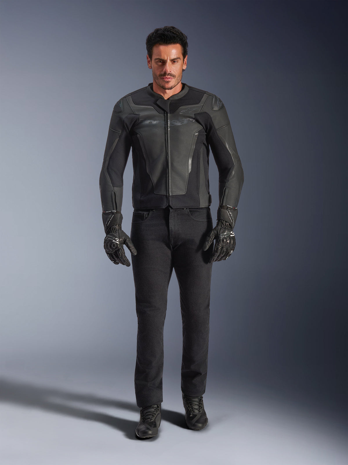 Alpinestars GP Force V2 läderjacka i svart, bärs av en manlig förare med svarta motorcykelbyxor, handskar och stövlar, stilren läderkonstruktion i sportstil med axel-sliders och integrerat skydd.