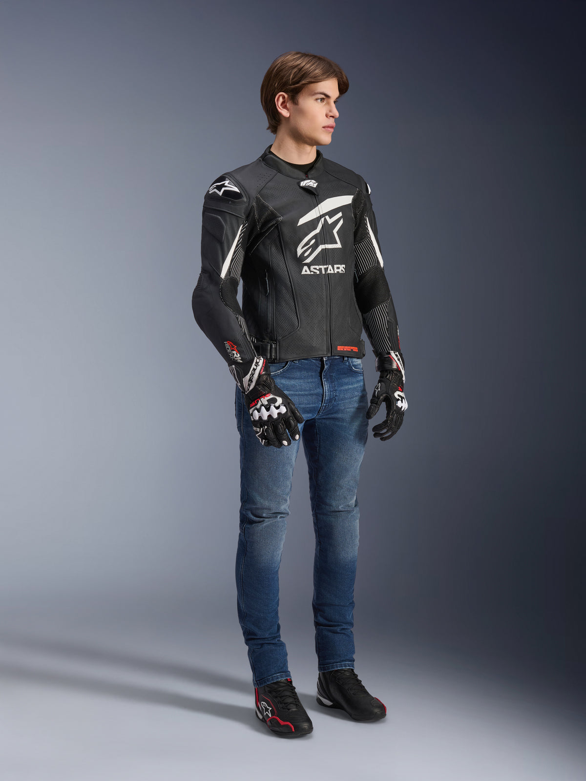Alpinestars GP Plus R V4 Rideknit läderjacka, svart och vit, motorcykeljacka i läder som bärs av en modell med blå jeans och svarta handskar, med en framträdande vit Astars-logotyp på bröstet, perforerade paneler och vita detaljer på axlarna.