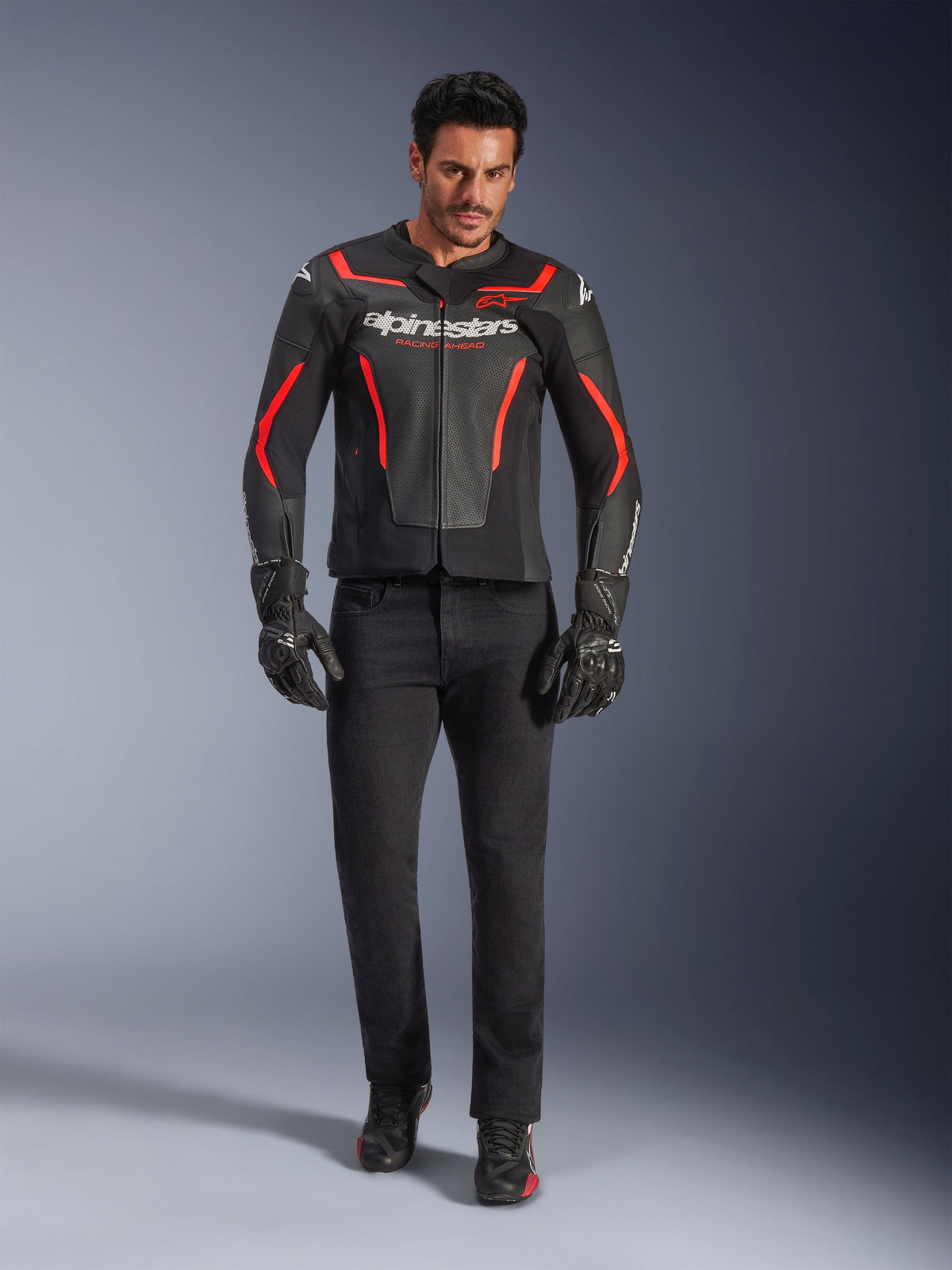 Manlig motorcyklist klädd i Alpinestars GP Force V2 Air läderjacka, svart och röd fluo, tillsammans med svarta mc-jeans, handskar och skor, med perforerad läderkonstruktion, vit logotyp och stilrena röda accenter för en sportig look