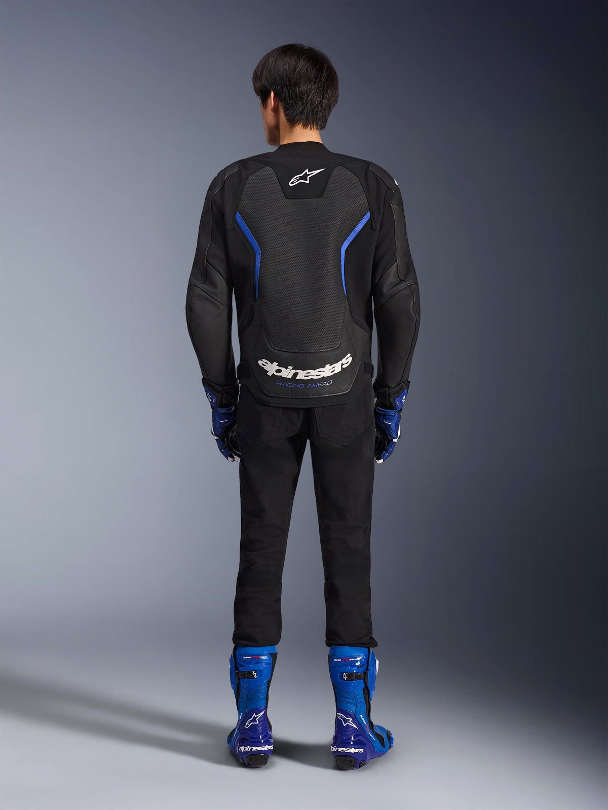 Alpinestars GP Force V2 Airflow läderjacka, Black Metallic Blue, vy bakifrån som visar perforerade läderpaneler och vit logotyp, bärs med blå racingstövlar och svarta byxor, sportig racingutrustning för motorcykel