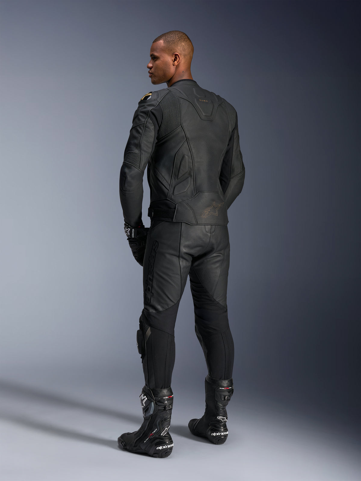 Alpinestars Dusk läderjacka, svart racingjacka för herr, ryggvy på modell i skinnställ, premiumläder med 3D-konstruktion.