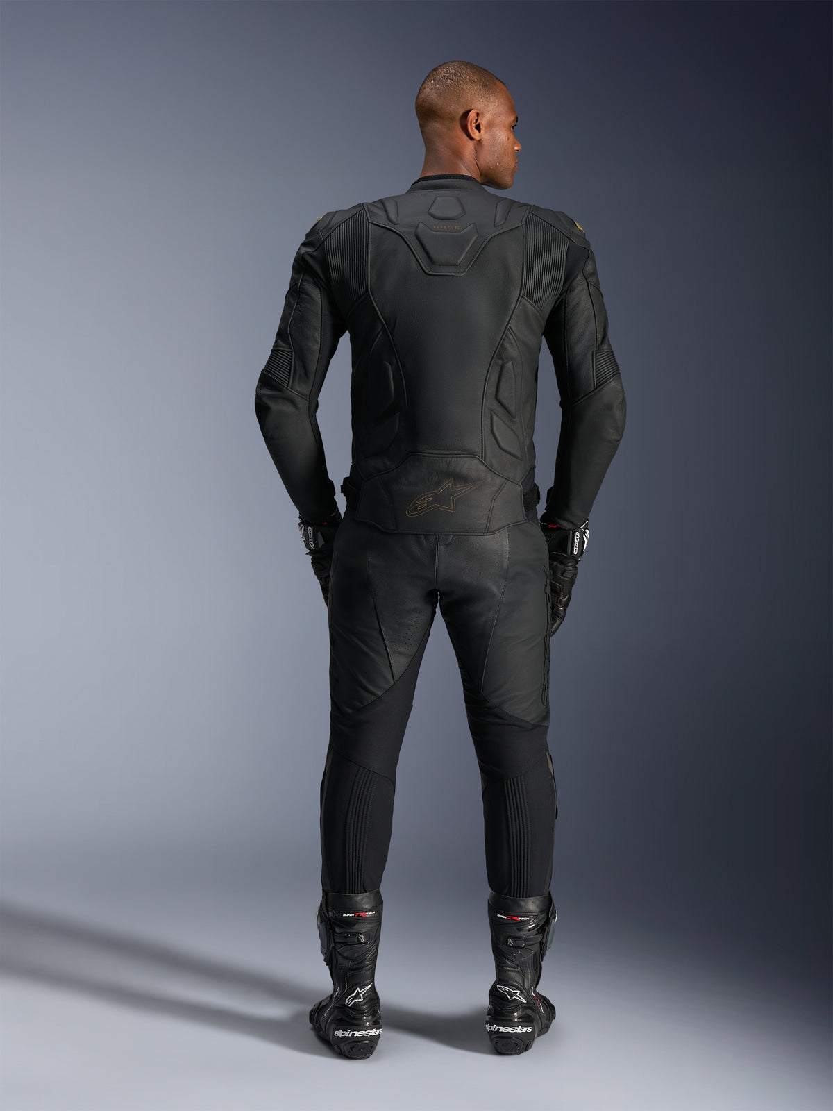 Alpinestars Dusk läderjacka, svart motorcykelracingjacka i nötläder, sedd bakifrån på en förare i skyddsutrustning.