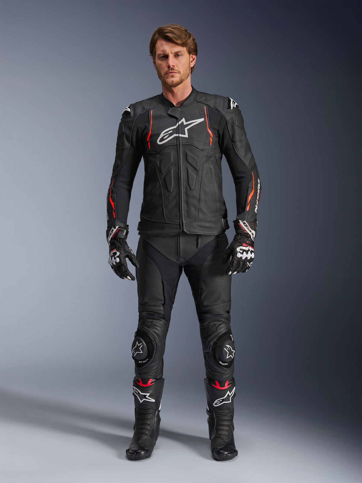 Manlig förare bärande Alpinestars Dusk Airflow läderjacka i Black Red Fluo, med perforerade läderpaneler och en vit logotyp på bröstet, matchad med svarta motorcykelbyxor i läder, knäpuckar, handskar och racingstövlar, komplett motorcykelutrustning.