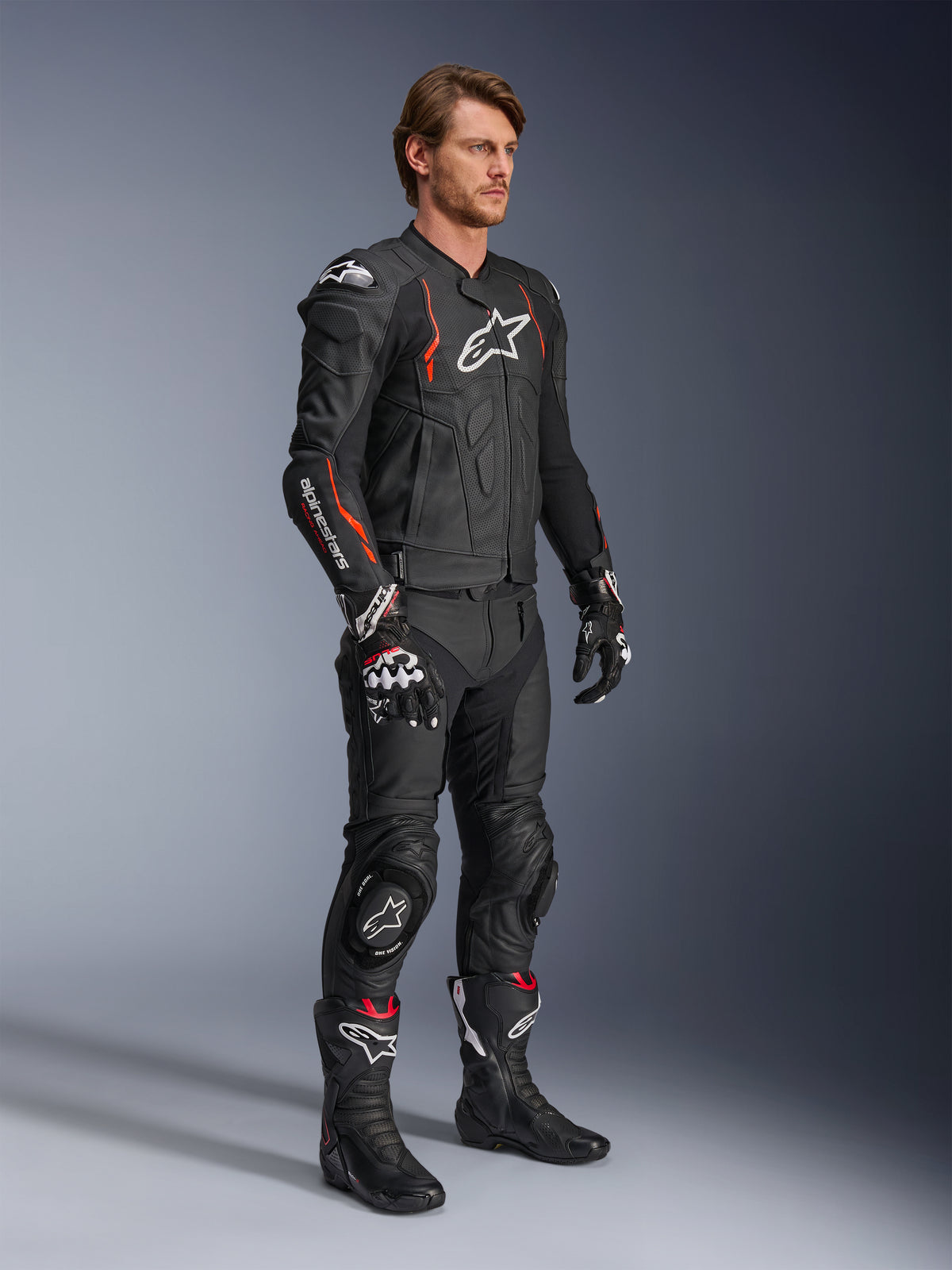 Alpinestars Dusk Airflow läderjacka, Black Red Fluo, bärs som en del av en komplett racingoutfit för motorcykel med matchande läderbyxor, handskar och stövlar, med perforerad läderkonstruktion och sportiga detaljer.