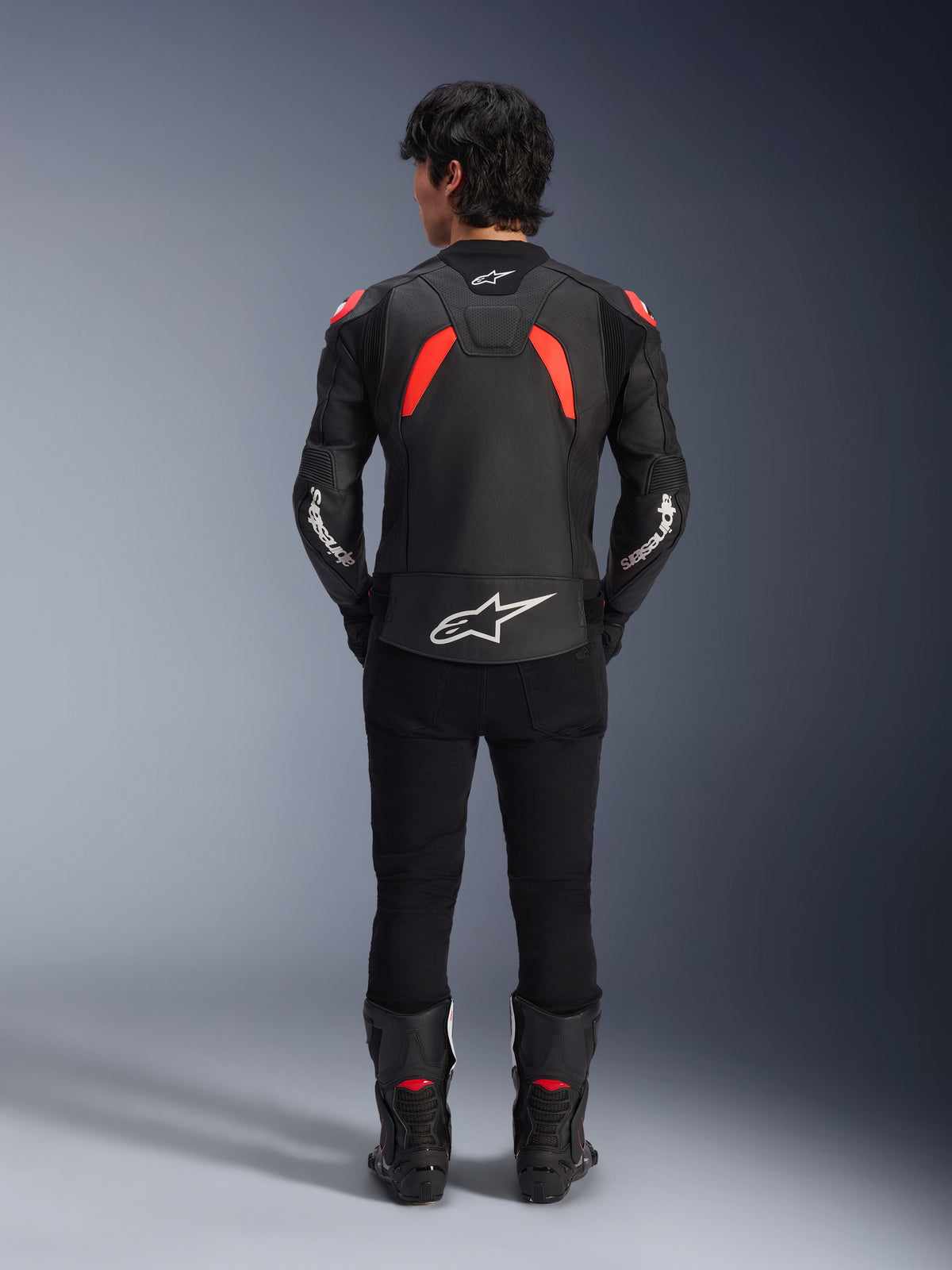 Alpinestars GP Plus R V4 Airflow läderjacka, svart, röd fluo och vit, vy bakifrån på en modell, med perforerade läderpaneler och framträdande vita logotyper, matchad med svarta motorcykelbyxor och stövlar