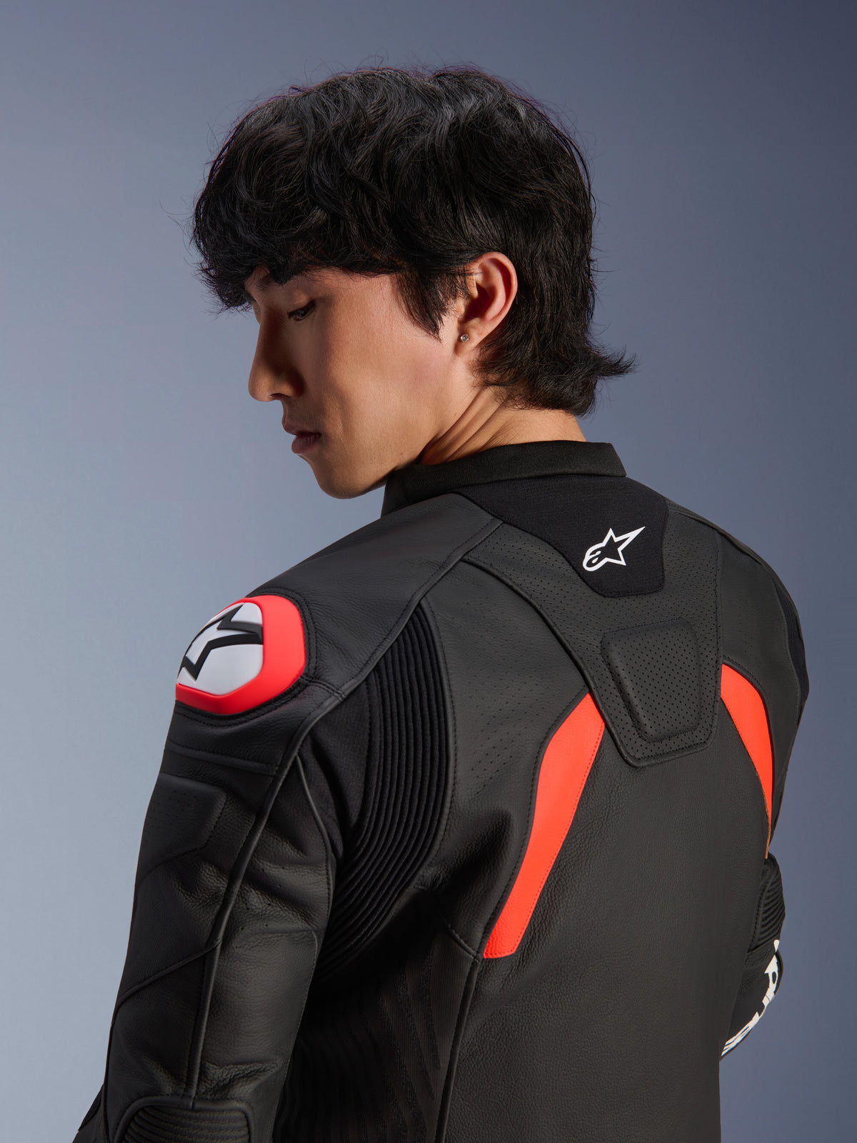 Alpinestars GP Plus R V4 Airflow läderjacka, svart med röd fluo och vita detaljer, närbild på rygg och axel på en modell, med perforerade läderzoner, Alpinestars-logotyp och integrerat axelskydd för motorcykelprestanda.