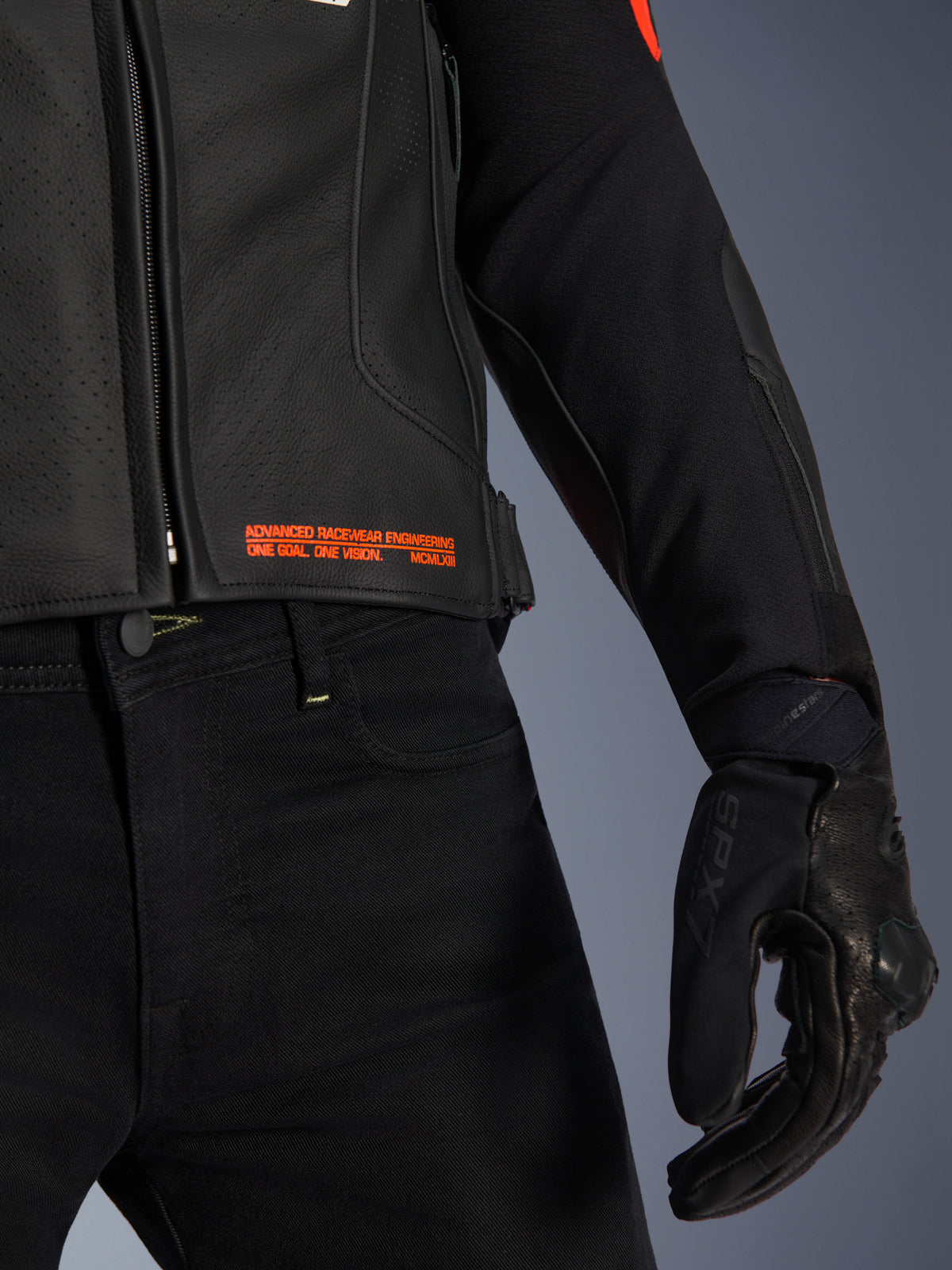 Alpinestars GP Plus R V4 Airflow läderjacka, närbild på midja och ärm, svart perforerat läder med röd fluo-text 'Advanced Racewear Engineering', kombinerat med svarta mc-byxor och SPX 7 motorcykelhandske.
