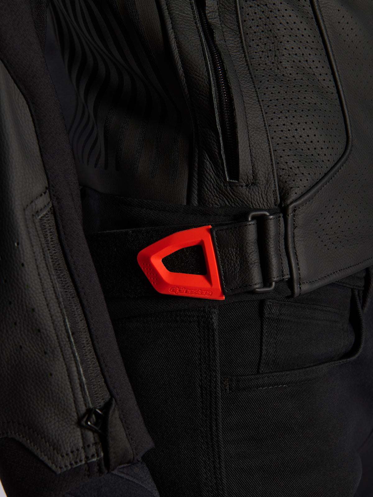 Alpinestars GP Plus R V4 Airflow läderjacka i närbild, svart perforerat läder med en lysande röd fluo-midjejustering med kardborreband, sidoficka med dragkedja och ergonomiska texturerade paneler.