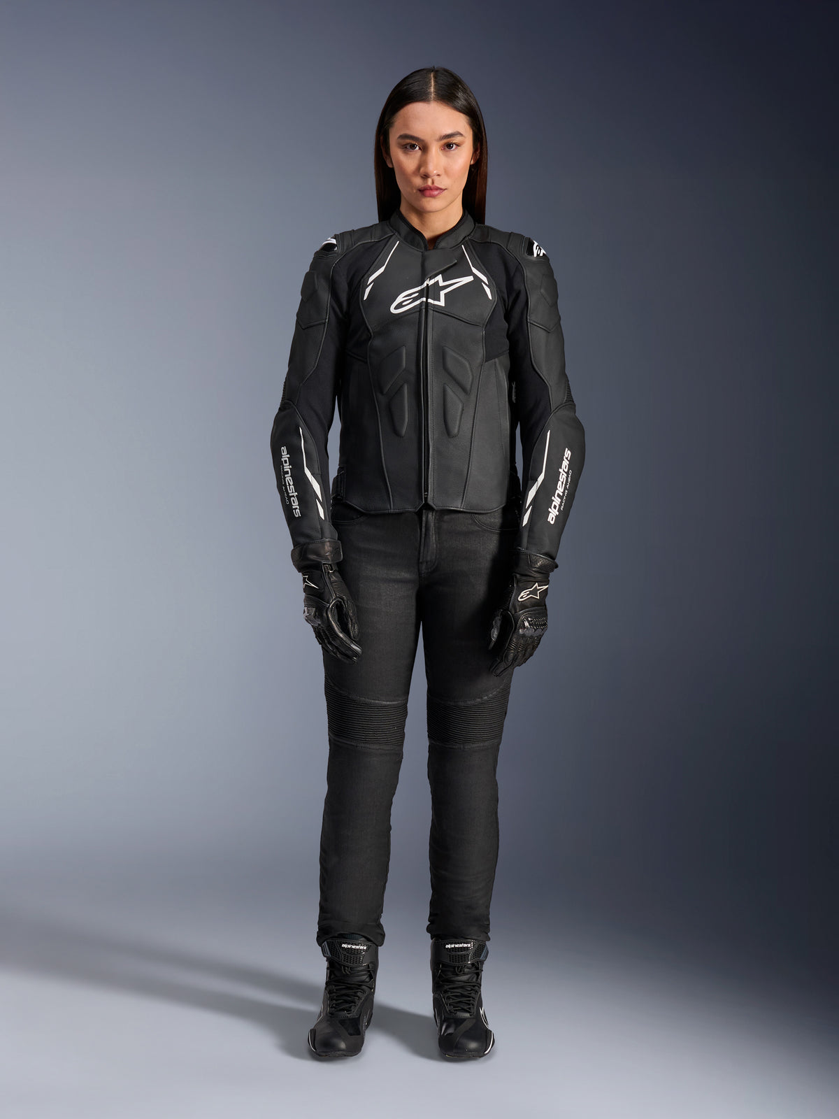 Alpinestars Stella Dusk läderjacka för dam, svart och vit, bärs av en modell med matchande svarta byxor och stövlar, vy framifrån, vita Alpinestars-logotyper på bröstet och ärmarna, skyddsutrustning i premium nötläder för damer