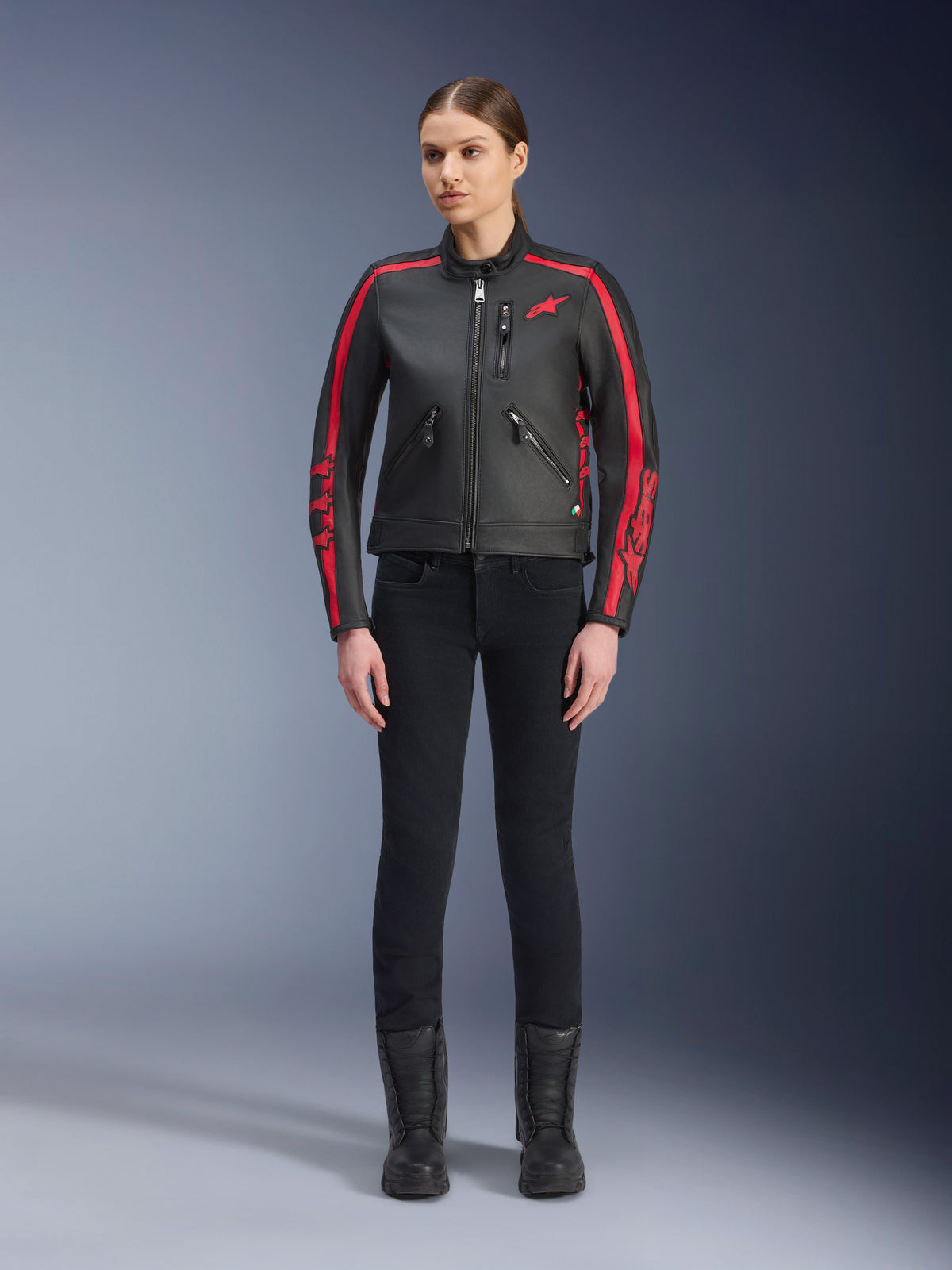 Alpinestars Stella Dyno läderjacka, mc-jacka för dam, svart och röd, med röda racingränder på axlar och ärmar, röd stjärnlogotyp på bröstet, bärs med svarta slim-fit-byxor och stövlar, premium nötläder med en modern heritage-design