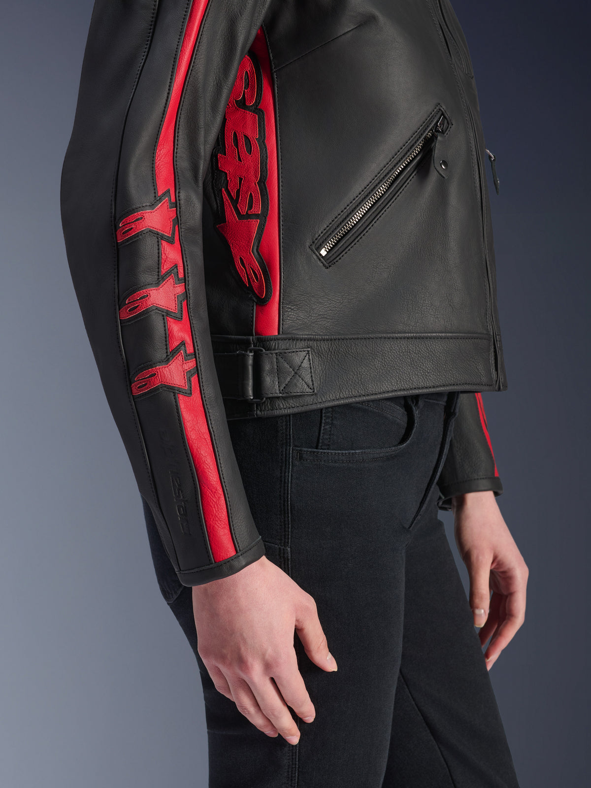 Alpinestars Stella Dyno läderjacka, motorcykeljacka för dam, svart och röd, sidovy buren av en modell, med röda racingränder och stjärnlogotyper på ärmen och en stor röd logotyp på sidan, premium nötläder, urban körstil