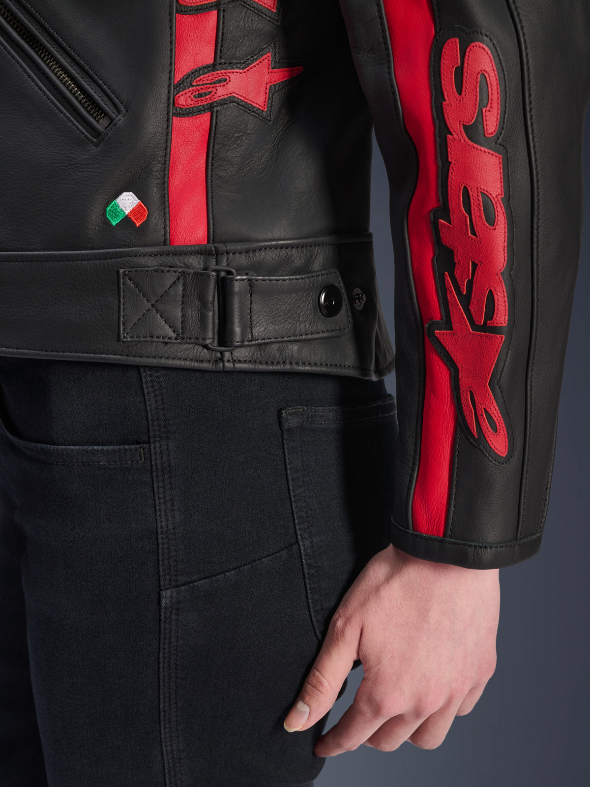 Alpinestars Stella Dyno läderjacka, motorcykeljacka i läder för dam, Black Haute Red, närbild av midja och ärm, röda racingränder med Alpinestars-logotyp, justerbar midjerem, litet italienskt flaggbroderi, konstruktion i premium nötläder