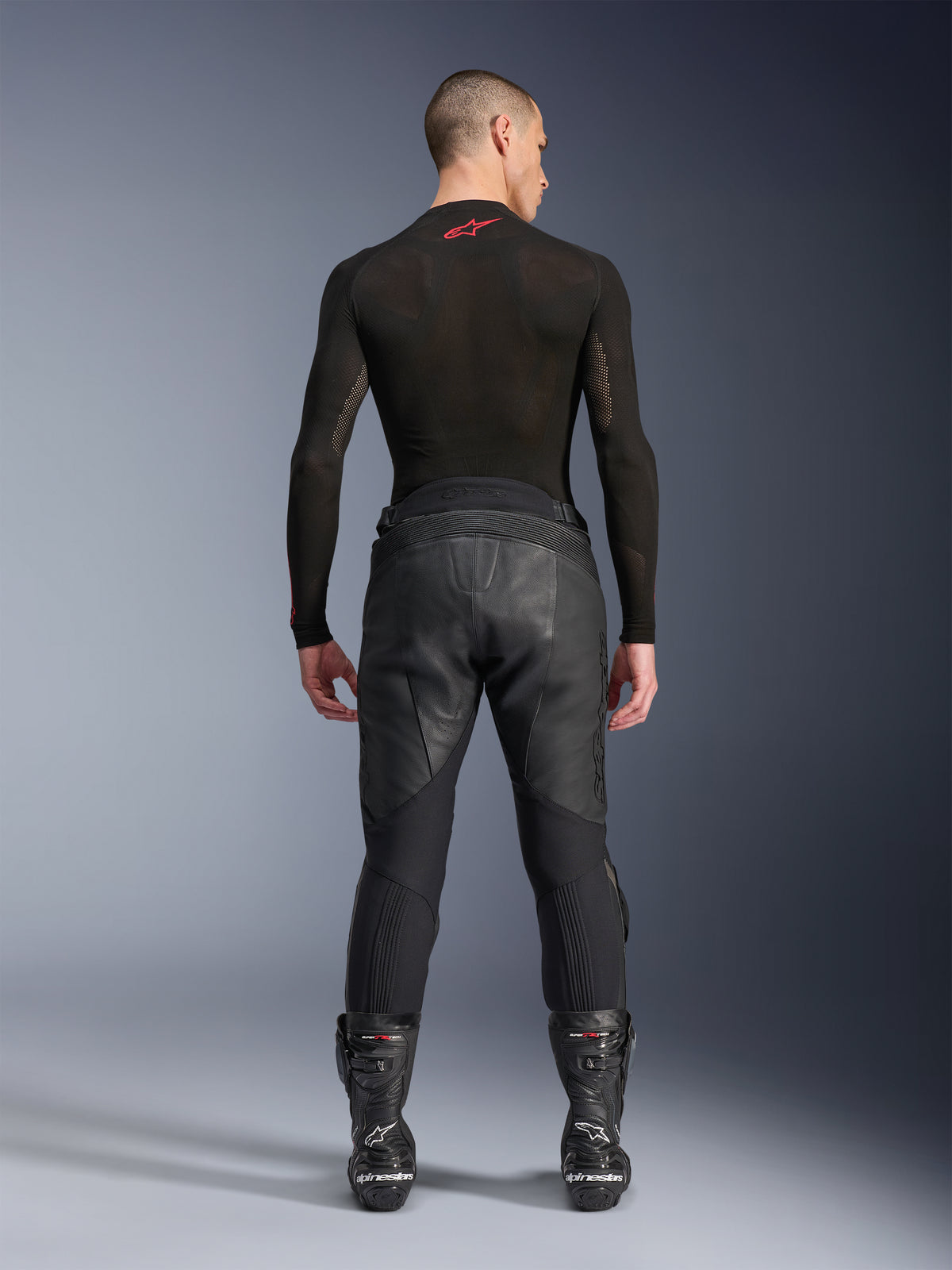 Alpinestars Missile V3 Läderbyxor, svarta, vy bakifrån på modell som bär en svart långärmad kompressionströja och racingstövlar, premiumläderkonstruktion med hög midjeöverlappning och stretchzoner, professionell motorcykelutrustning för racing