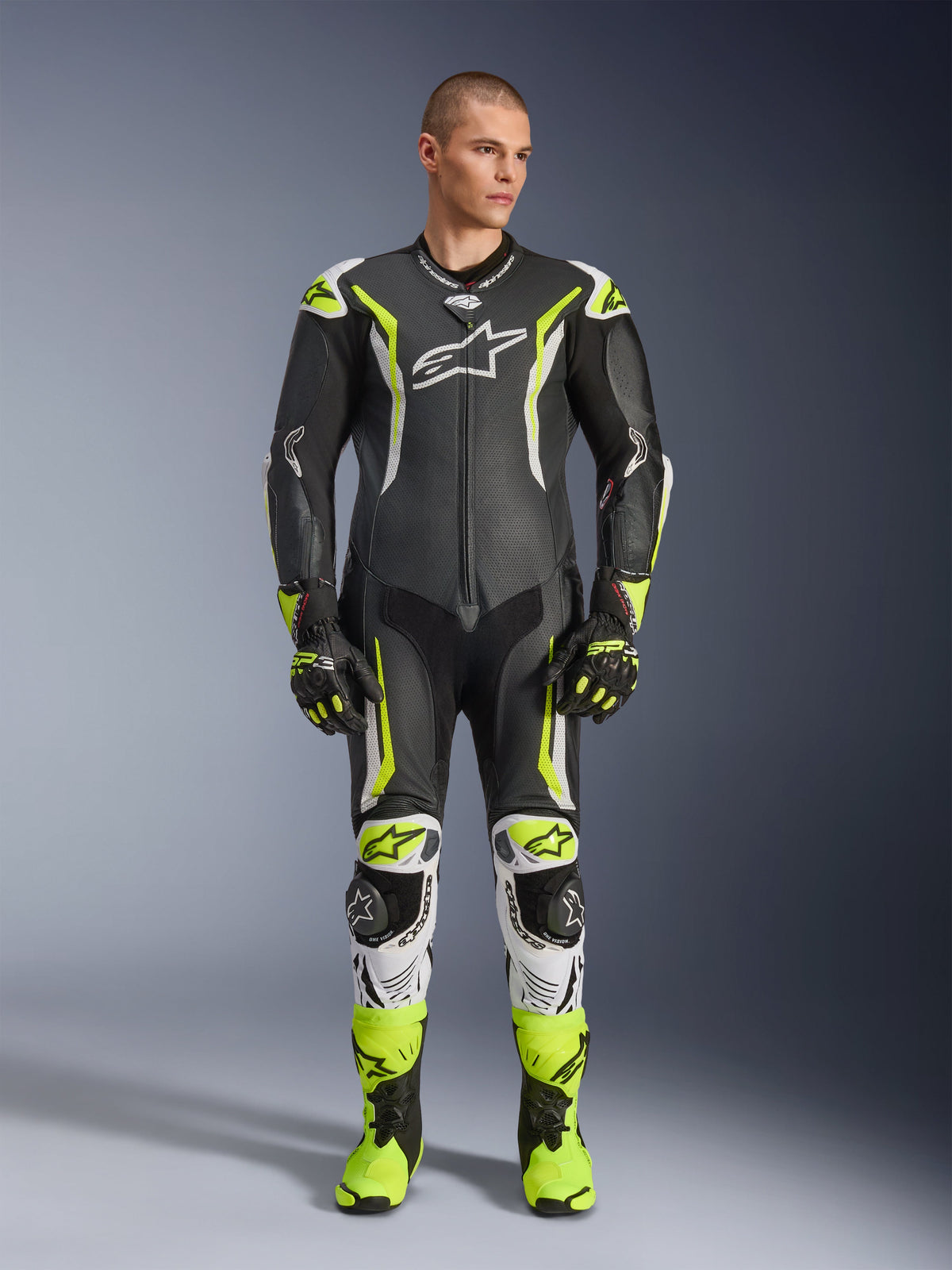 Alpinestars GP Tech V5 One Piece Leather Suit, professional motorcycle racing suit in black and neon yellow fluo with white accents, worn by a model with matching racing gloves and boots, featuring an aerodynamic design and protective sliders.