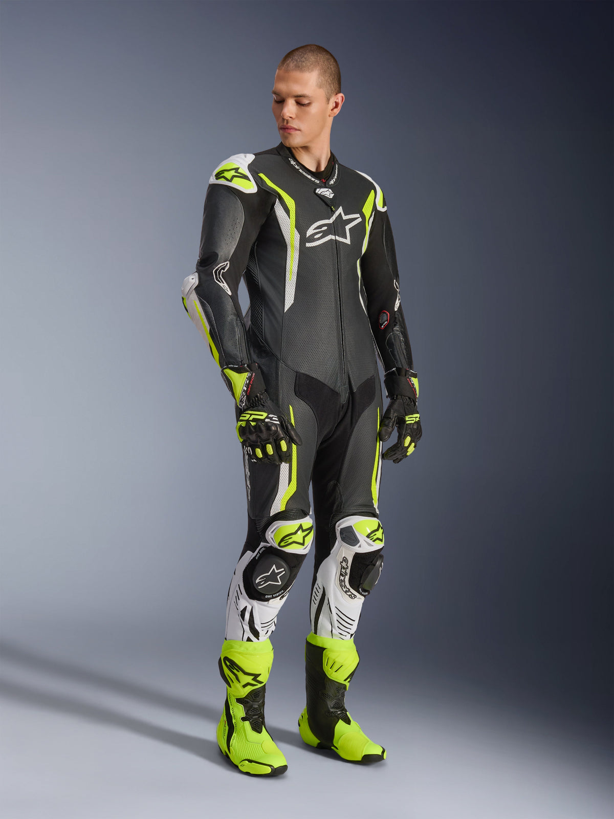 Alpinestars GP Tech V5 One Piece Leather Suit, Black White and Yellow Fluo, worn by a model with matching racing gloves and boots, professional motorcycle racing gear featuring aerodynamic performance and protective armor.