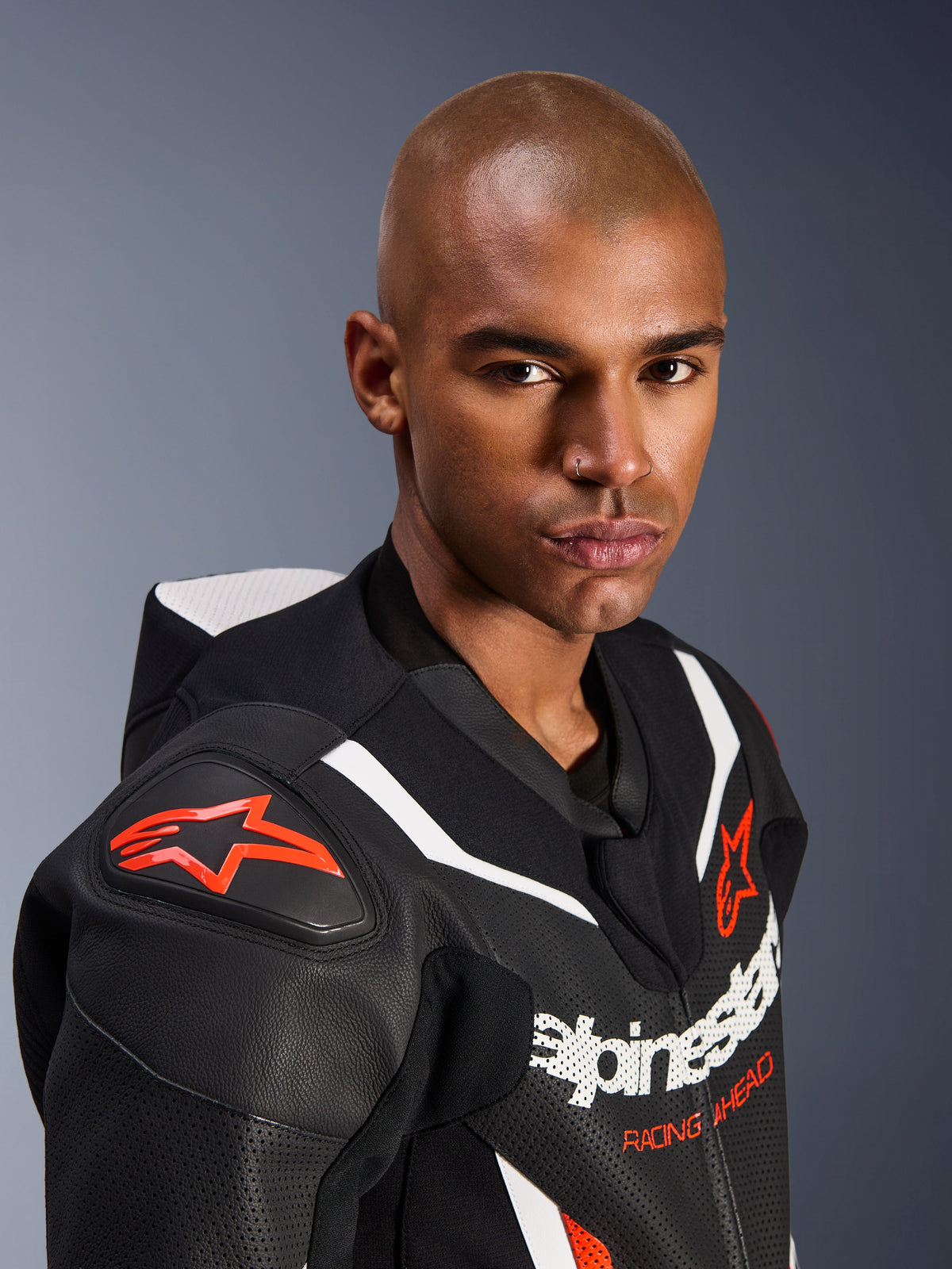 Close-up portrait of a model wearing the Alpinestars GP Force V2 Leather Suit, 1-Piece, Black White and Red Fluo, featuring perforated leather panels, white racing stripes, and red Alpinestars logos on the shoulder and chest.