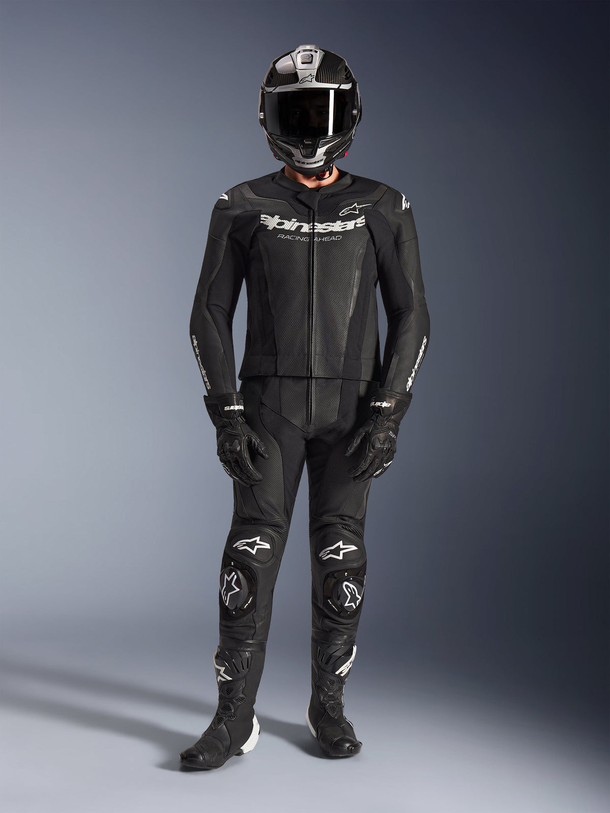 Alpinestars GP Force V2 2-Piece Leather Suit, Black, full-body motorcycle racing gear including a black helmet, gloves, and boots, featuring perforated leather panels and white Alpinestars logos on the chest and knees, designed for high-performance track riding.