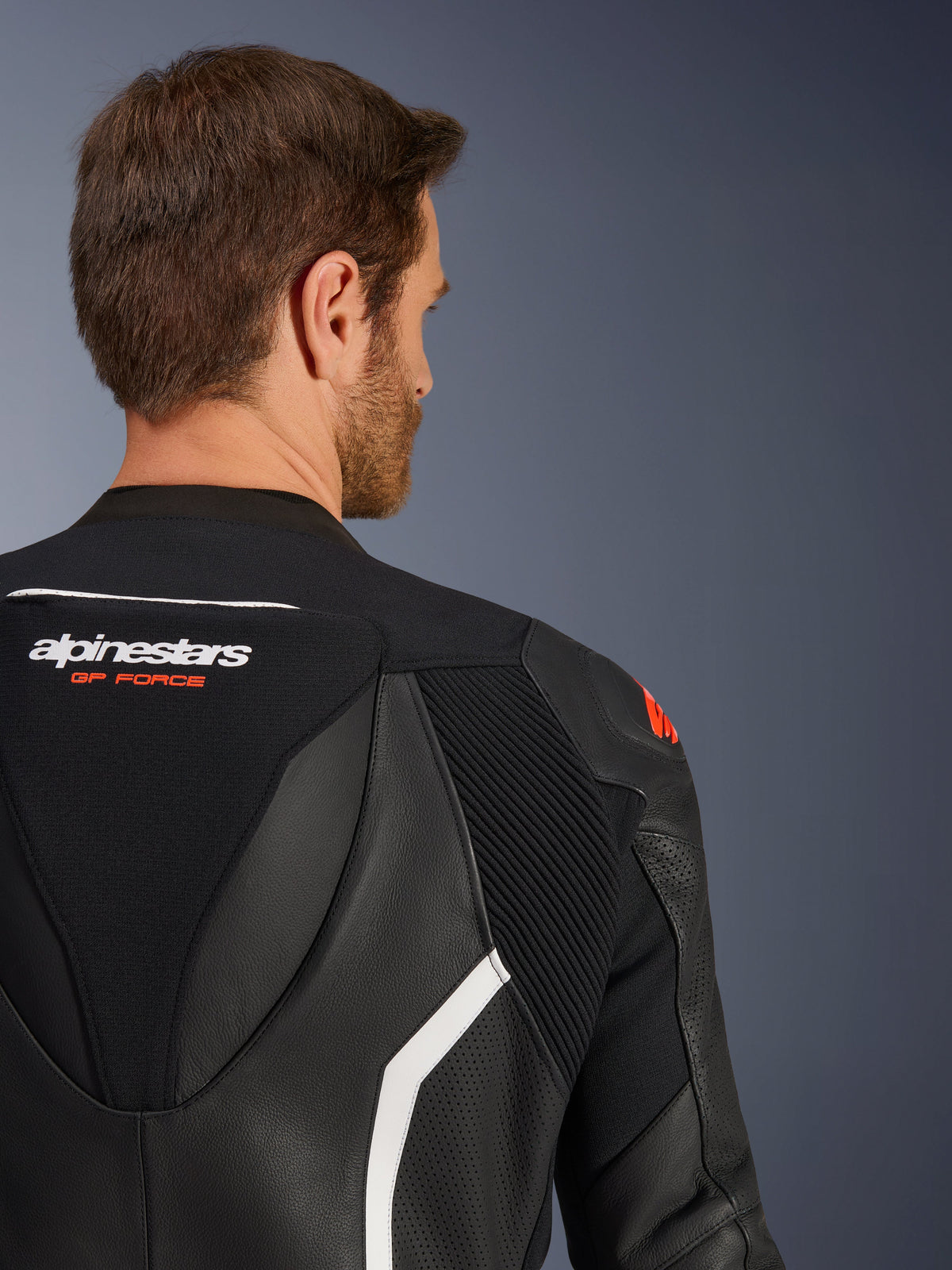 GP Force V2 2-Piece Leather Suit, close-up of the upper back and shoulder on a male model, black leather with white and red accents, Alpinestars GP Force branding, showing perforated panels and accordion stretch zones for motorcycle racing.