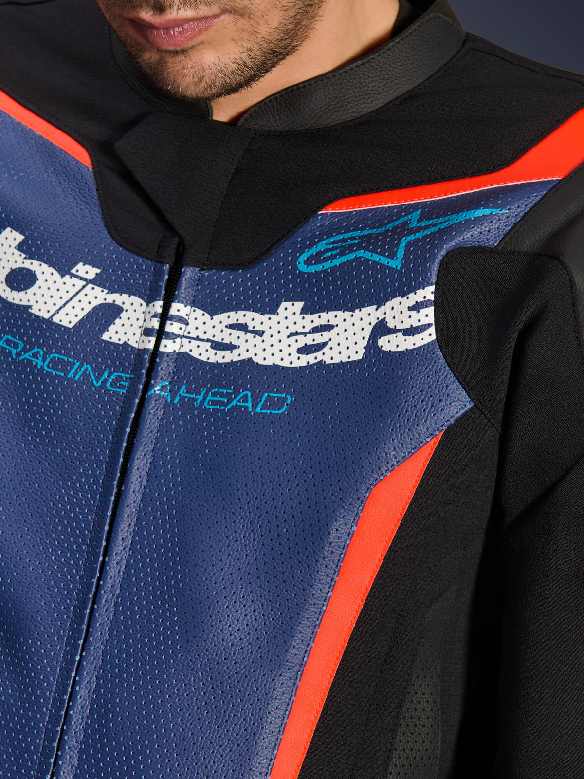 Alpinestars GP Force V2 Leather Suit, 2-Piece, Close-up of chest area, Perforated Blue leather with white logo and 'RACING AHEAD' text, Red Fluo accents and black panels, professional sport riding gear