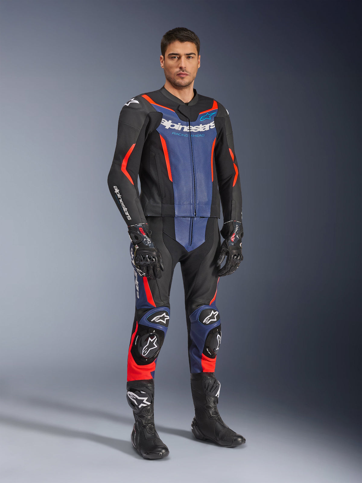 Alpinestars GP Force V2 tvådelat skinnställ, MC-ställ i läder, svart, blå och röd fluo, bärs med matchande svarta racinghandskar och stövlar, med perforerade paneler och skyddande sliders, aerodynamisk design för sportkörning
