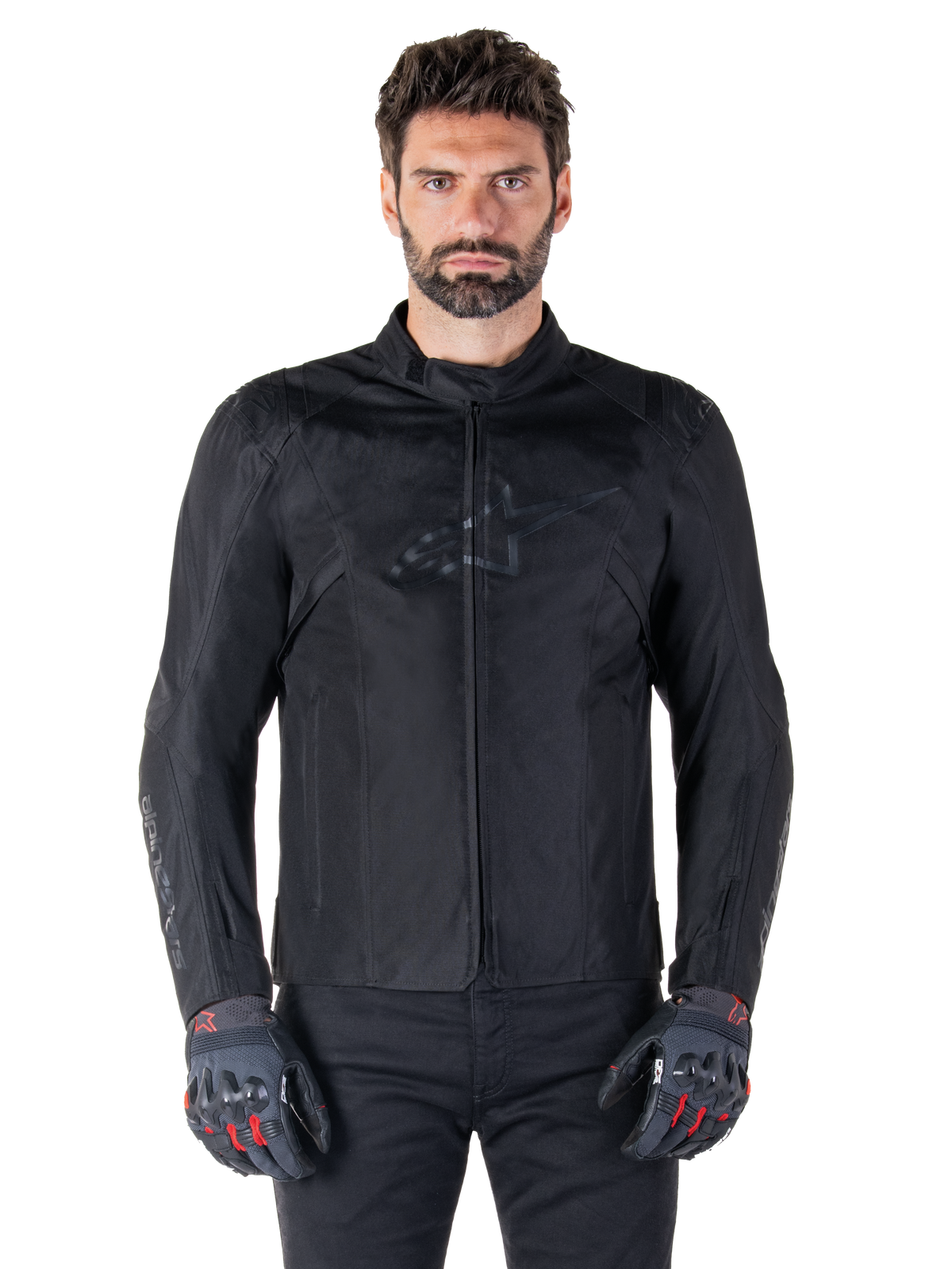 Alpinestars T-SPS V2 Waterproof Jacket, svart motorcykeljacka i textil, bärs av förare med svarta och röda handskar, med hög krage, dragkedja fram och diskret logotyp på bröstet, vattentätt skydd för sport- och stadskörning