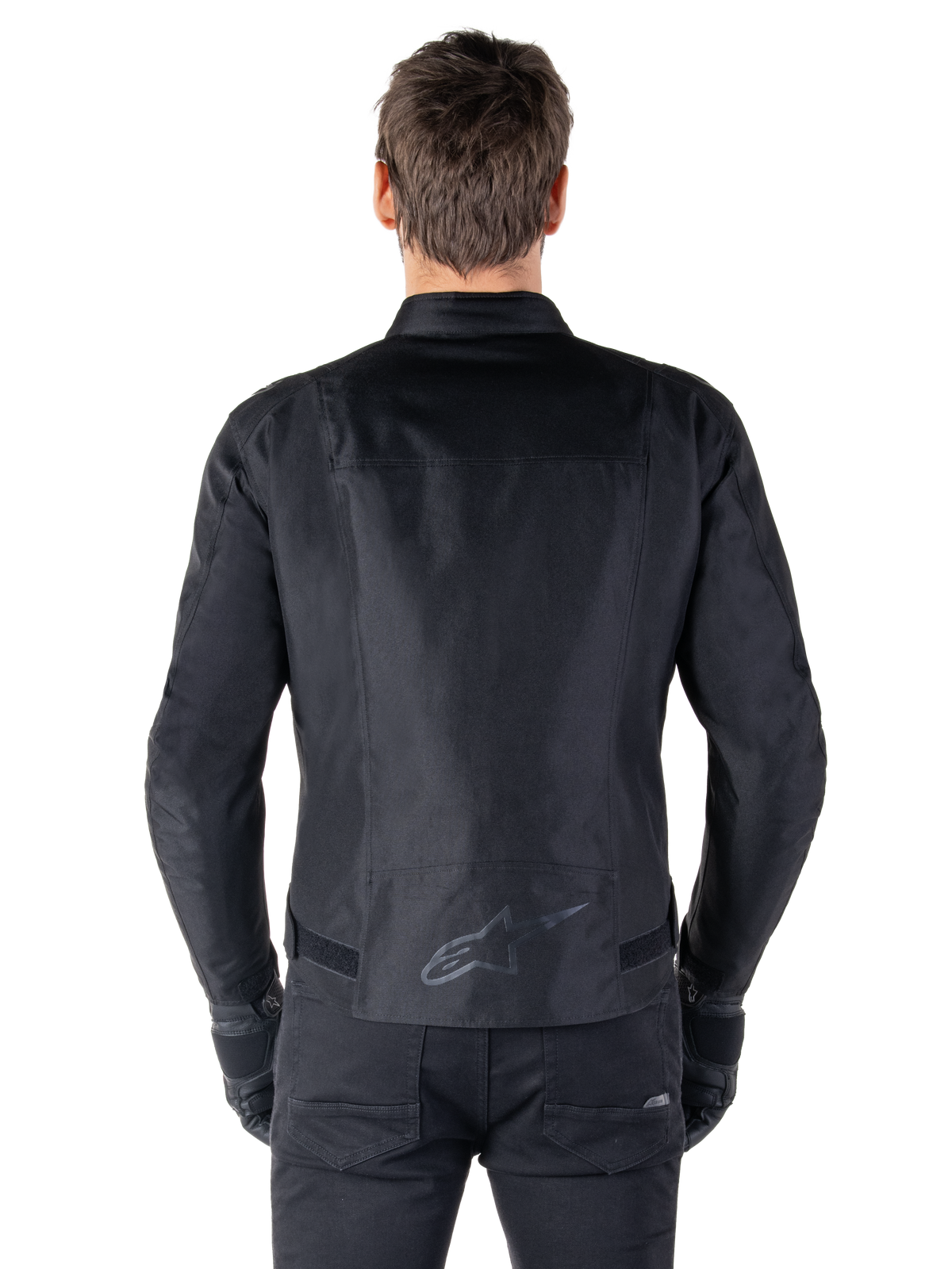 Alpinestars T-SPS V2 Waterproof Jacket, svart, sedd bakifrån som visar den sportiga siluetten, reflekterande Alpinestars-logotyp på nedre delen av ryggen och förlängt ryggparti för extra täckning vid körning