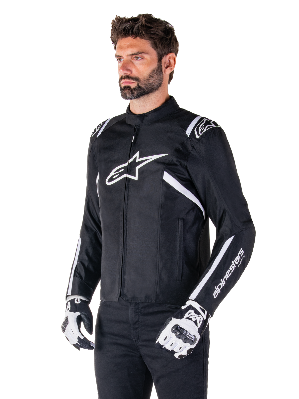 Alpinestars T-SPS V2 Waterproof Jacket, svart och vit, bärs av en manlig modell med matchande motorcykelhandskar, sportig textiljacka med vita Alpinestars-logotyper på bröst och axlar, 'alpinestars T-SPS'-logotyp på ärmen, stilren raceinspirerad motorcykelutrustning