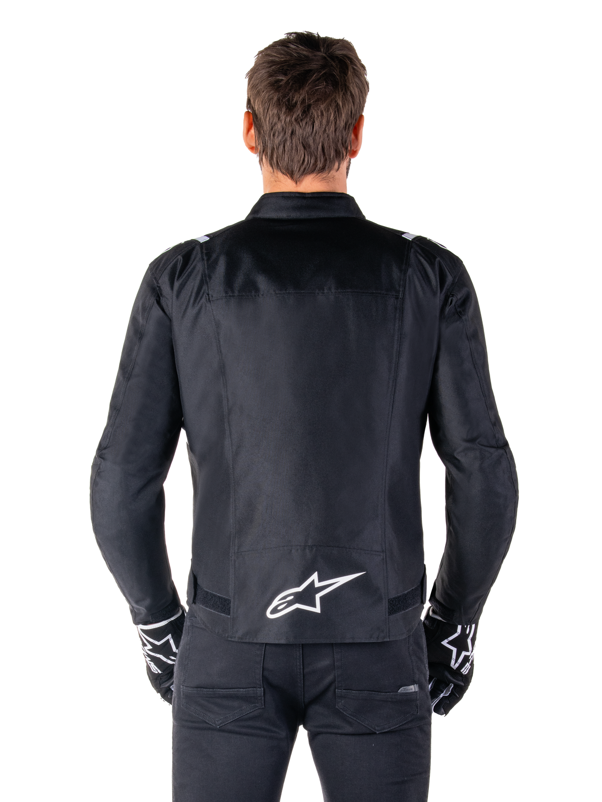 Alpinestars T-SPS V2 Waterproof Jacket, svart och vit, vy bakifrån som visar vit Alpinestars-logotyp på nedre delen av ryggen, bärs med svarta byxor och handskar, sportig textiljacka för motorcykel