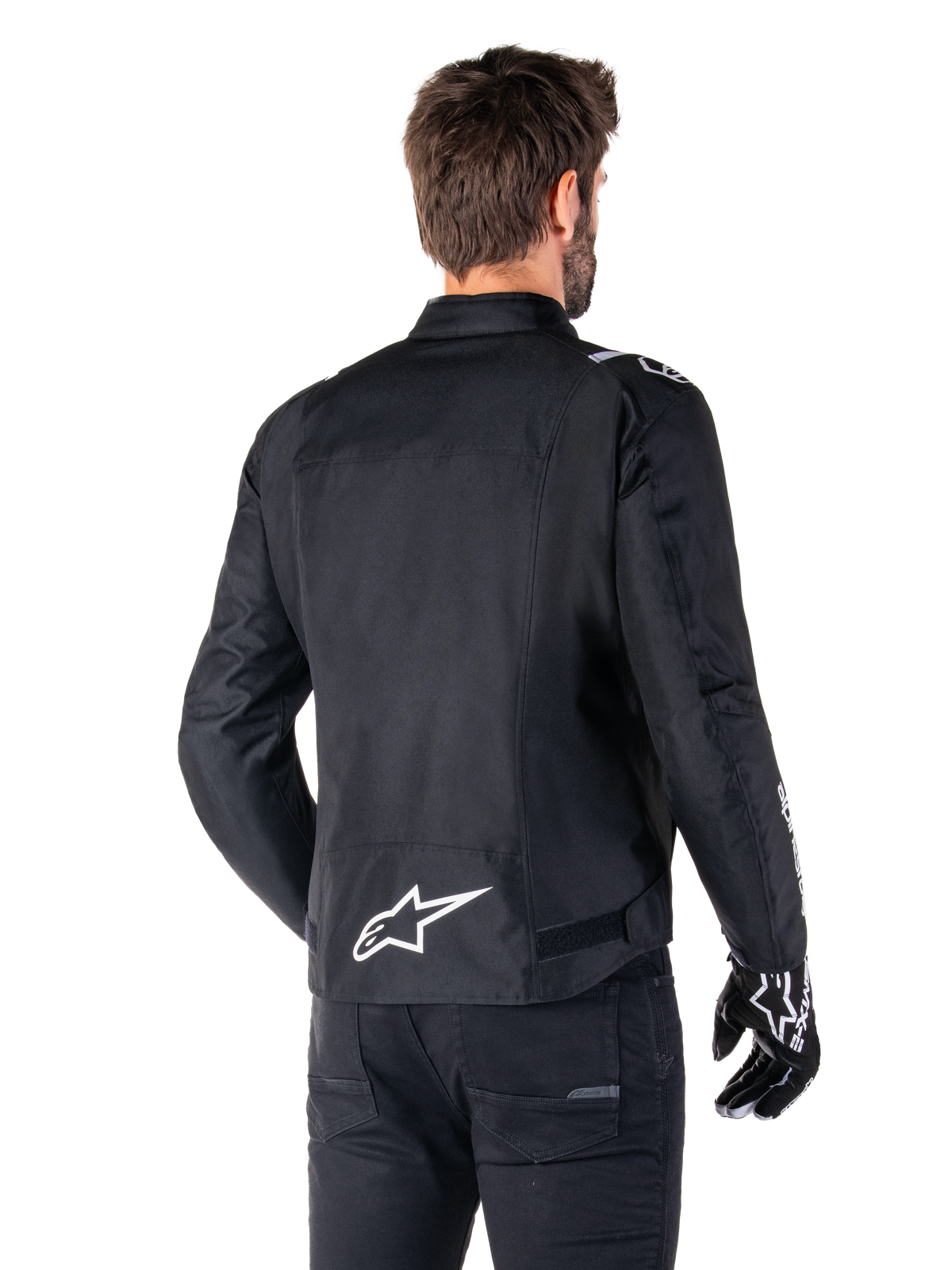 Alpinestars T-SPS V2 Waterproof Jacket, svart och vit, vy bakifrån på en manlig förare som bär jackan, vit Alpinestars-logotyp på nedre delen av ryggen, sportig textilkonstruktion, bärs med svarta körbyxor och handskar