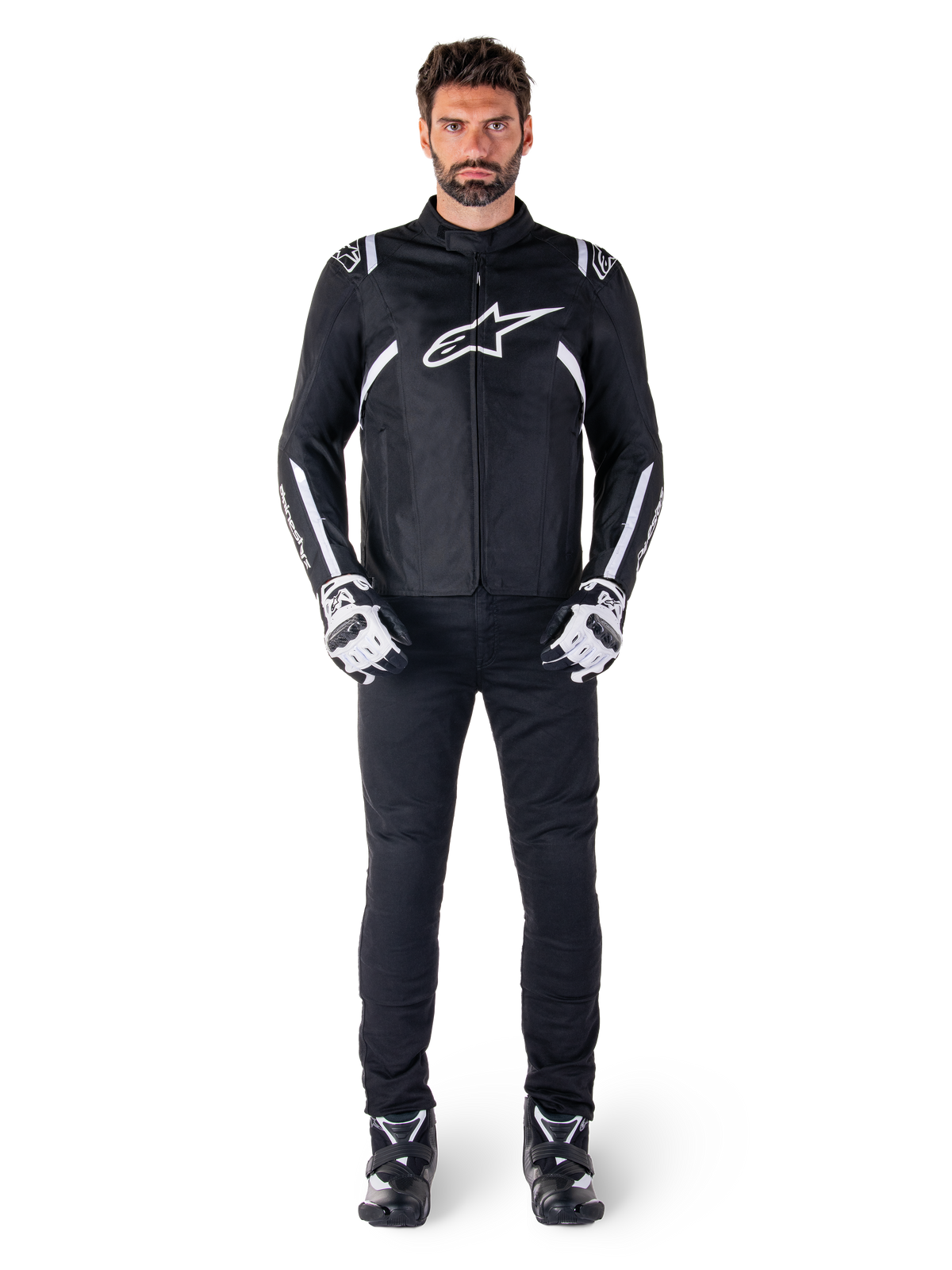 Alpinestars T-SPS V2 Waterproof Jacket, svart och vit, bärs av manlig modell med svarta byxor och matchande handskar, med vit Alpinestars-logotyp på bröstet och detaljer på ärmarna, sportig siluett för motorcykelkörning i alla väder