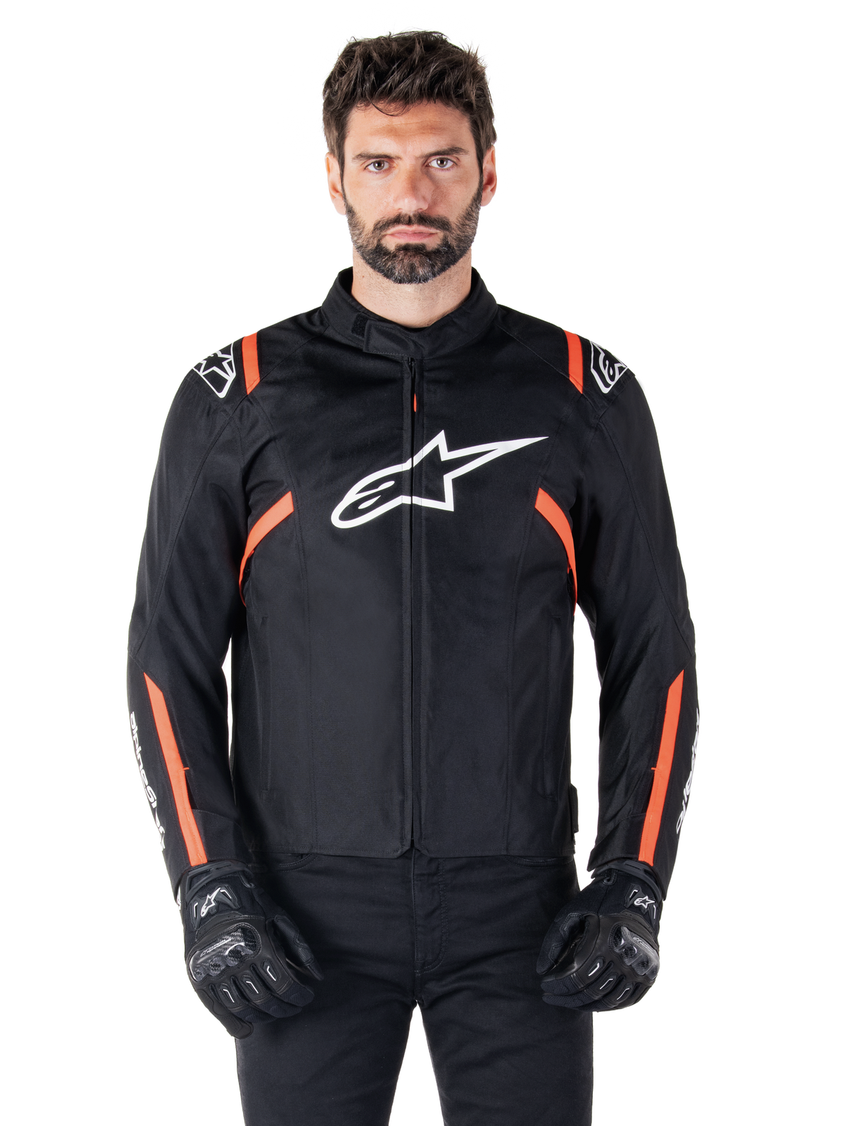 Alpinestars T-SPS V2 Waterproof-jacka, svart, vit och röd fluo, bärs av en manlig modell med svarta mc-handskar, med en stor vit Alpinestars-logotyp på bröstet och livfulla orangea detaljer på axlar och ärmar.