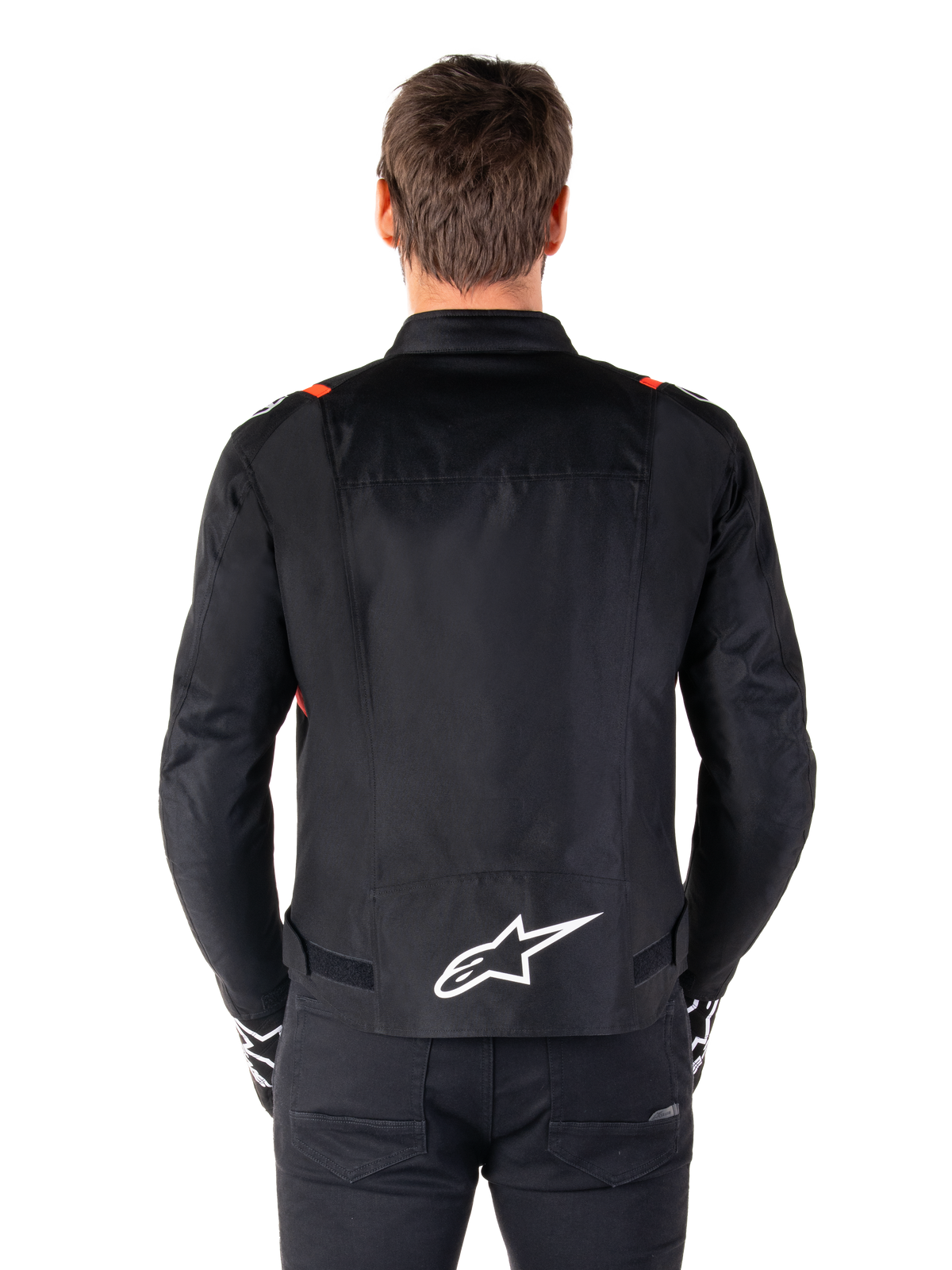 Alpinestars T-SPS V2 Waterproof-jacka, svart med vita och röd-fluo-detaljer, vy bakifrån med en stor vit Alpinestars-logotyp på nedre ryggen, sportig textiljacka för motorcykel, bärs med svarta byxor och handskar