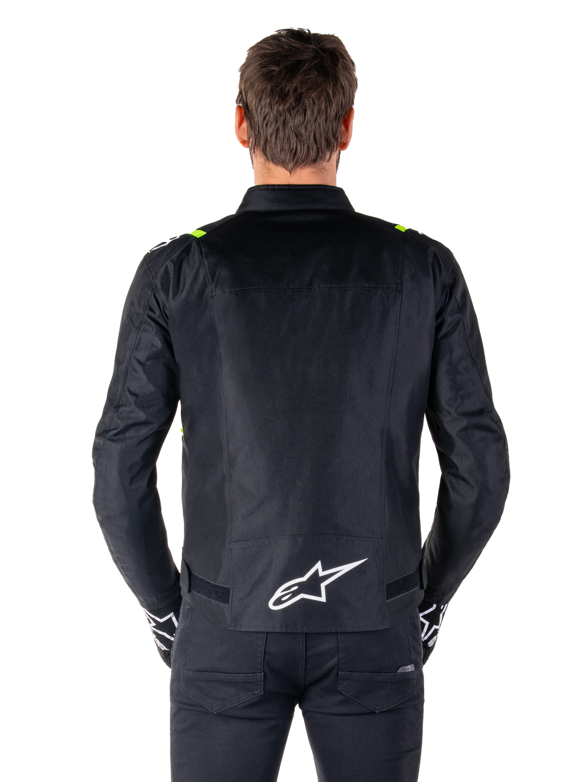 Alpinestars T-SPS V2 Waterproof Jacket, sedd bakifrån, svart med gula fluo-detaljer på axlarna och vit stjärnlogotyp på nedre delen av ryggen, textiljacka för motorcykel med sportig silhuett, bärs av en manlig modell.