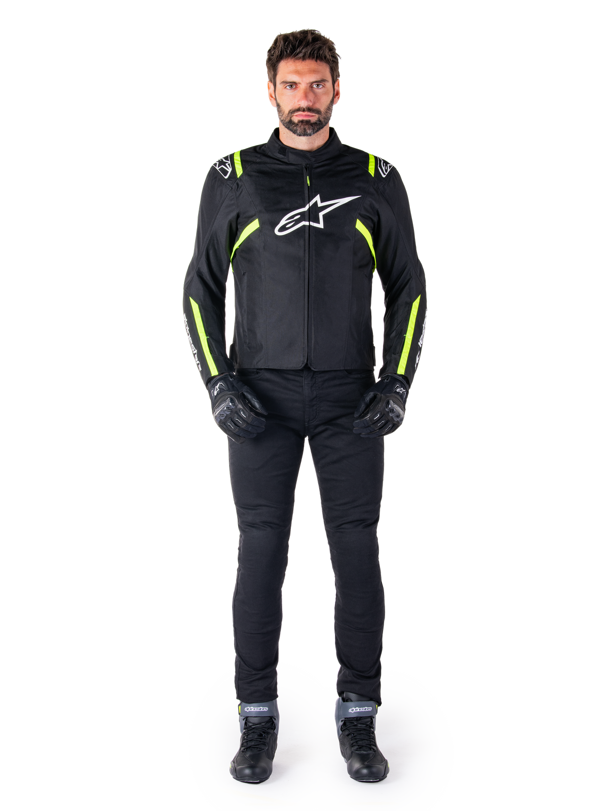 Alpinestars T-SPS V2 Vattentät Jacka, svart, vit och gul fluo, bärs av en modell med svarta körbyxor och handskar, vit Alpinestars-logotyp på bröstet och fluorescerande detaljer på axlar och ärmar, sportig motorcykelutrustning