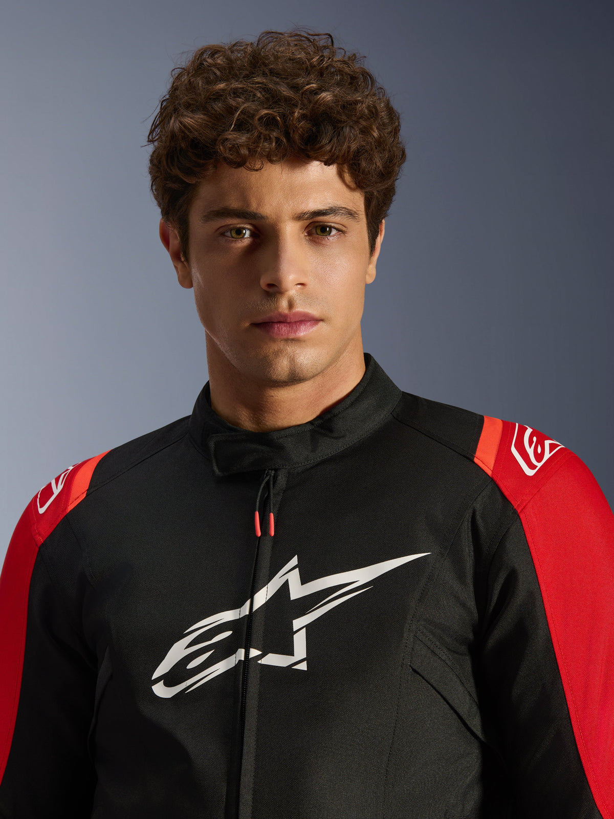 Manlig modell som bär Alpinestars T-SPS V2 Waterproof Jacket, svart med röda detaljer och vit logotyp, närbild i porträttvy, sportmotorcykeljacka i textil