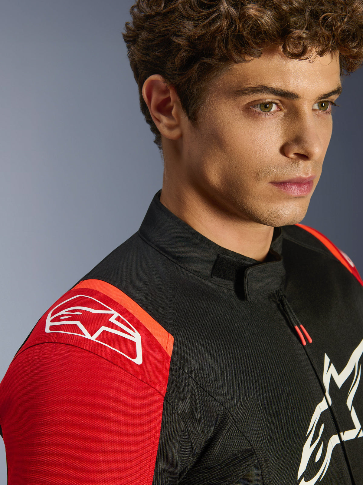 Alpinestars T-SPS V2 Waterproof-jacka, textiljacka för motorcykel, svart, röd och fluorescerande röd, närbild på modell som bär jackan, framträdande vita Alpinestars-logotyper på axel och bröst, lågprofilkrage och atletisk sportpassform